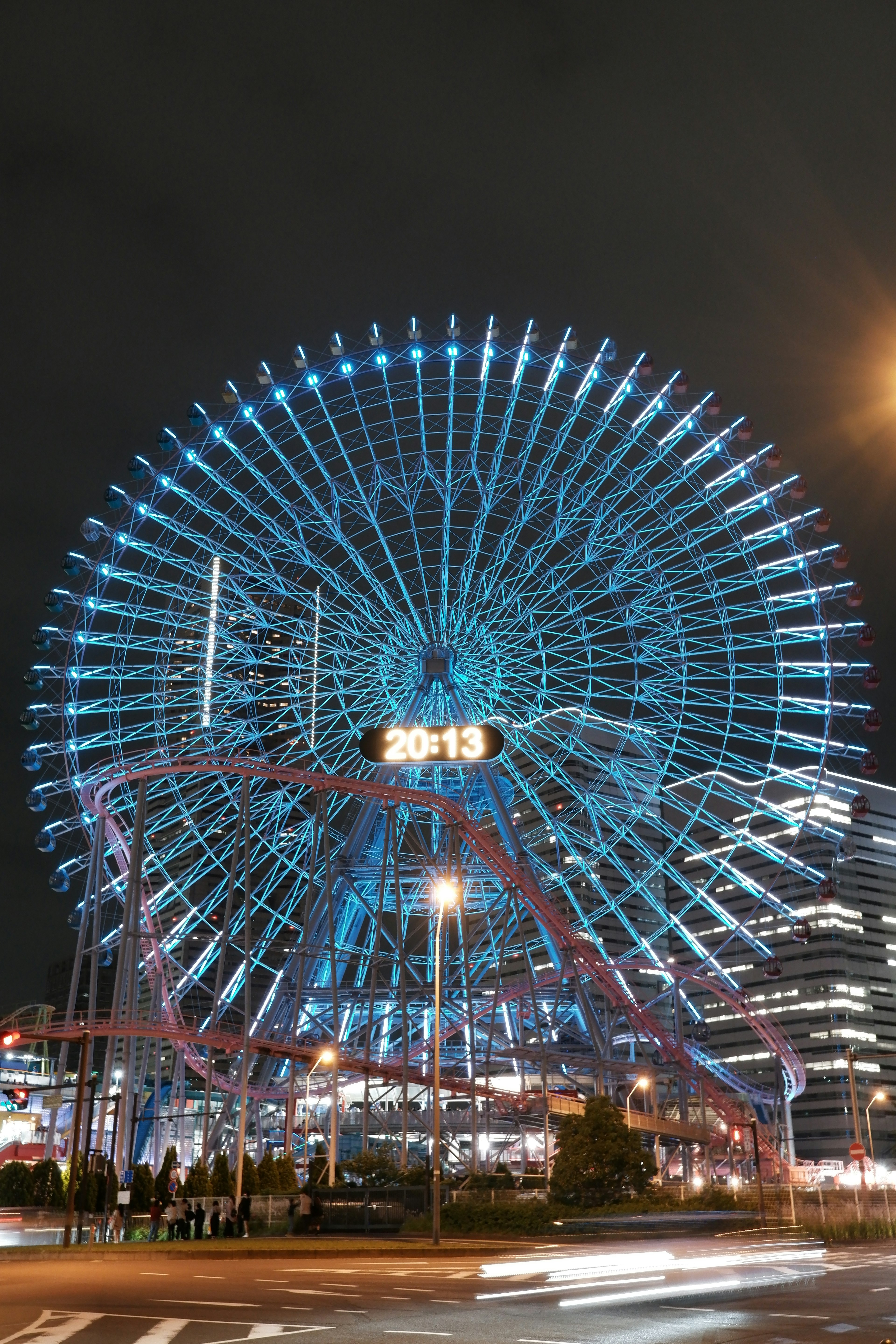 Una noria iluminada de azul con el horizonte de la ciudad de noche