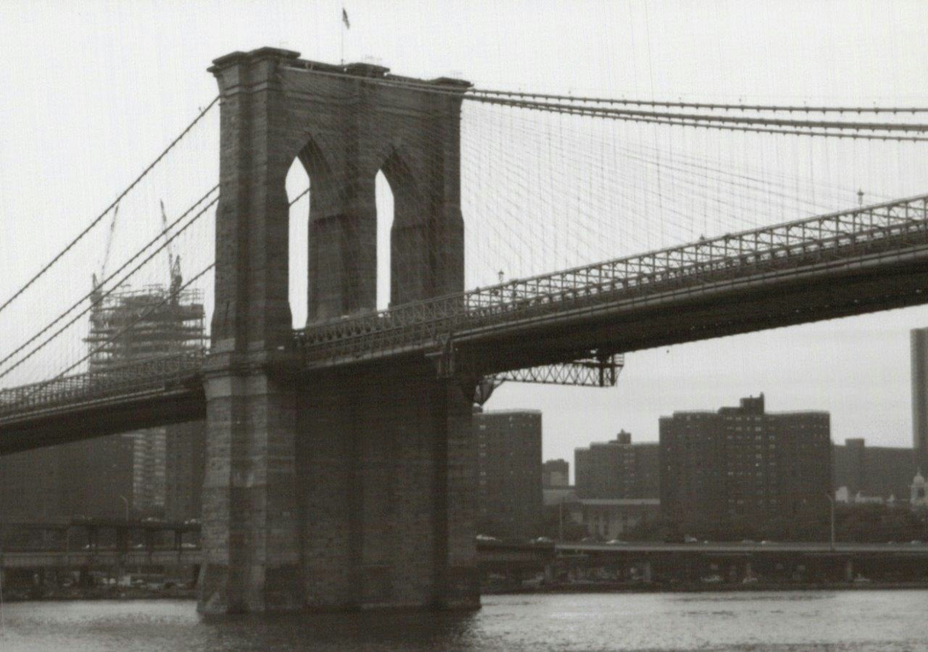 Schwarzweißfoto der Brooklyn Bridge mit Gebäuden und Wasseroberfläche