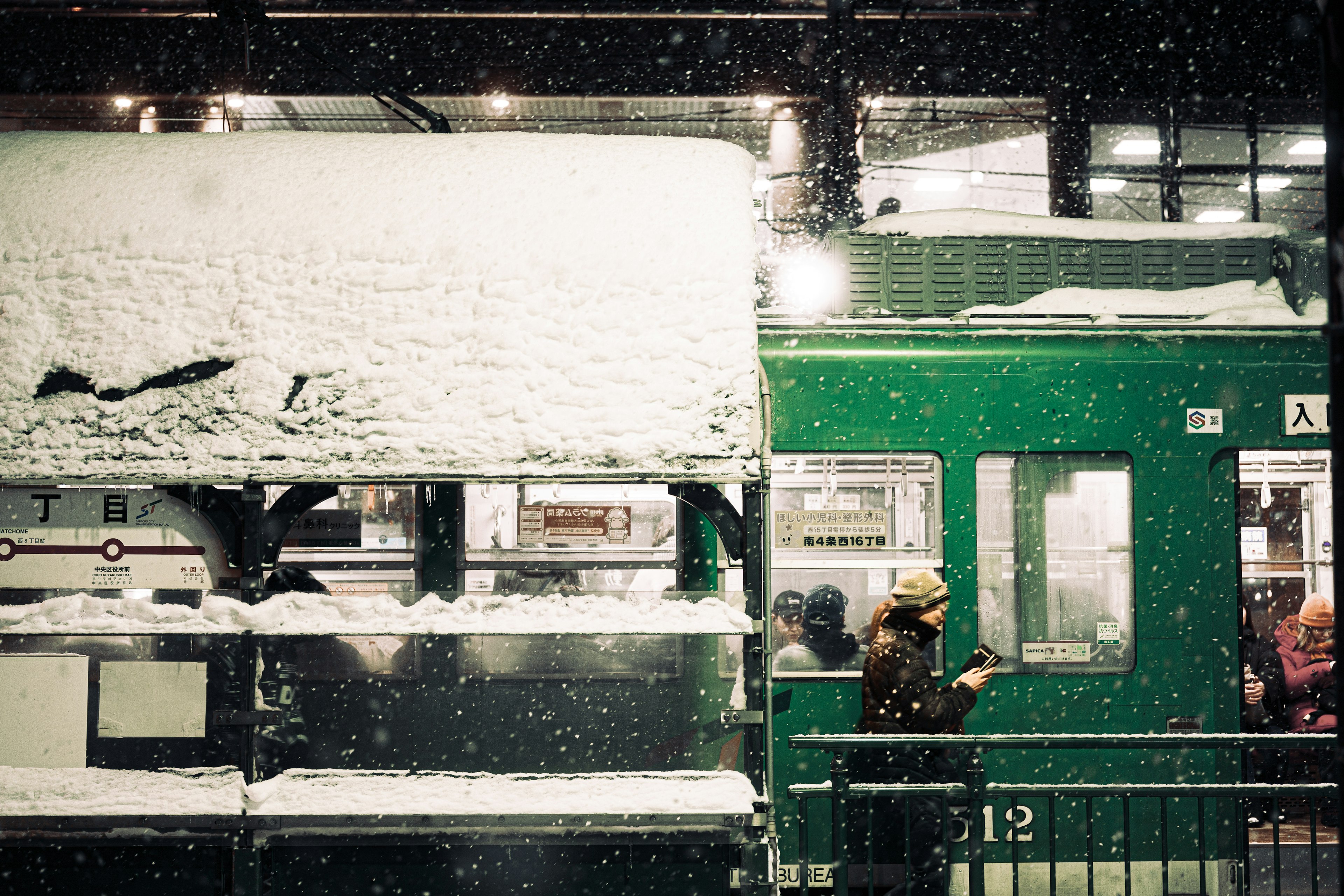 Schneebedeckter Bahnhof mit einem grünen Zug am Bahnsteig