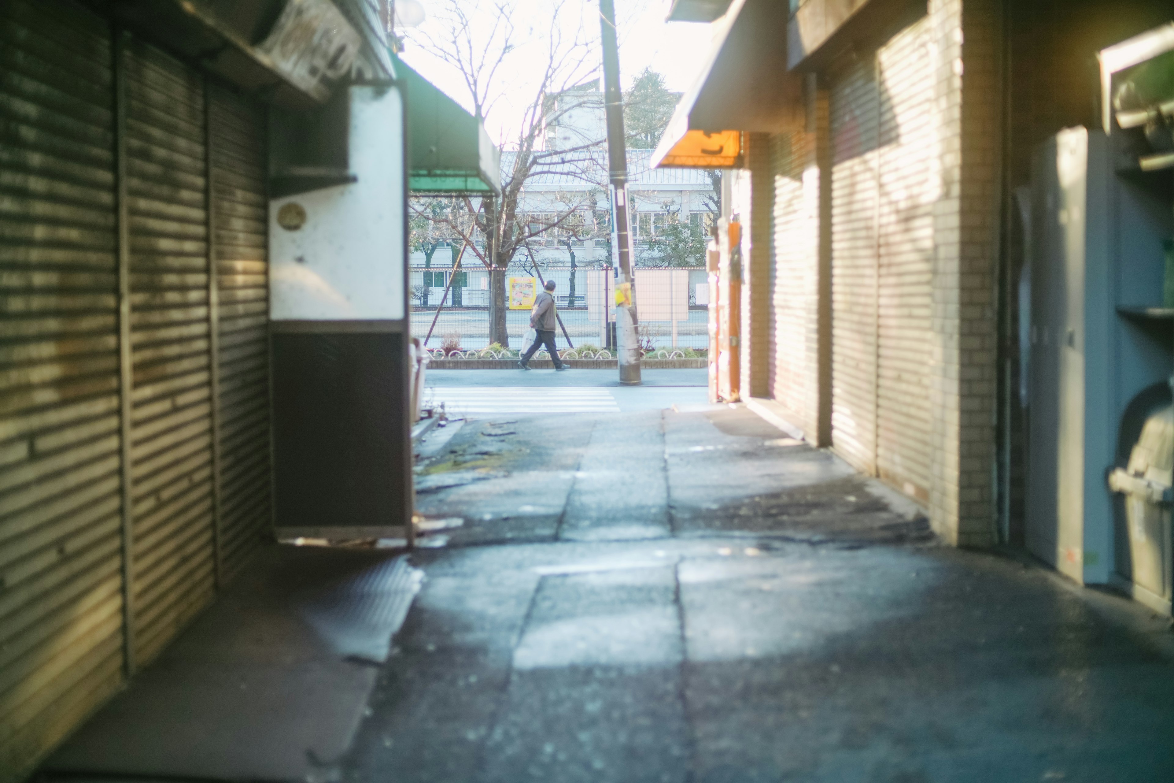 Escena de calle estrecha con una persona caminando y tiendas cerradas visibles