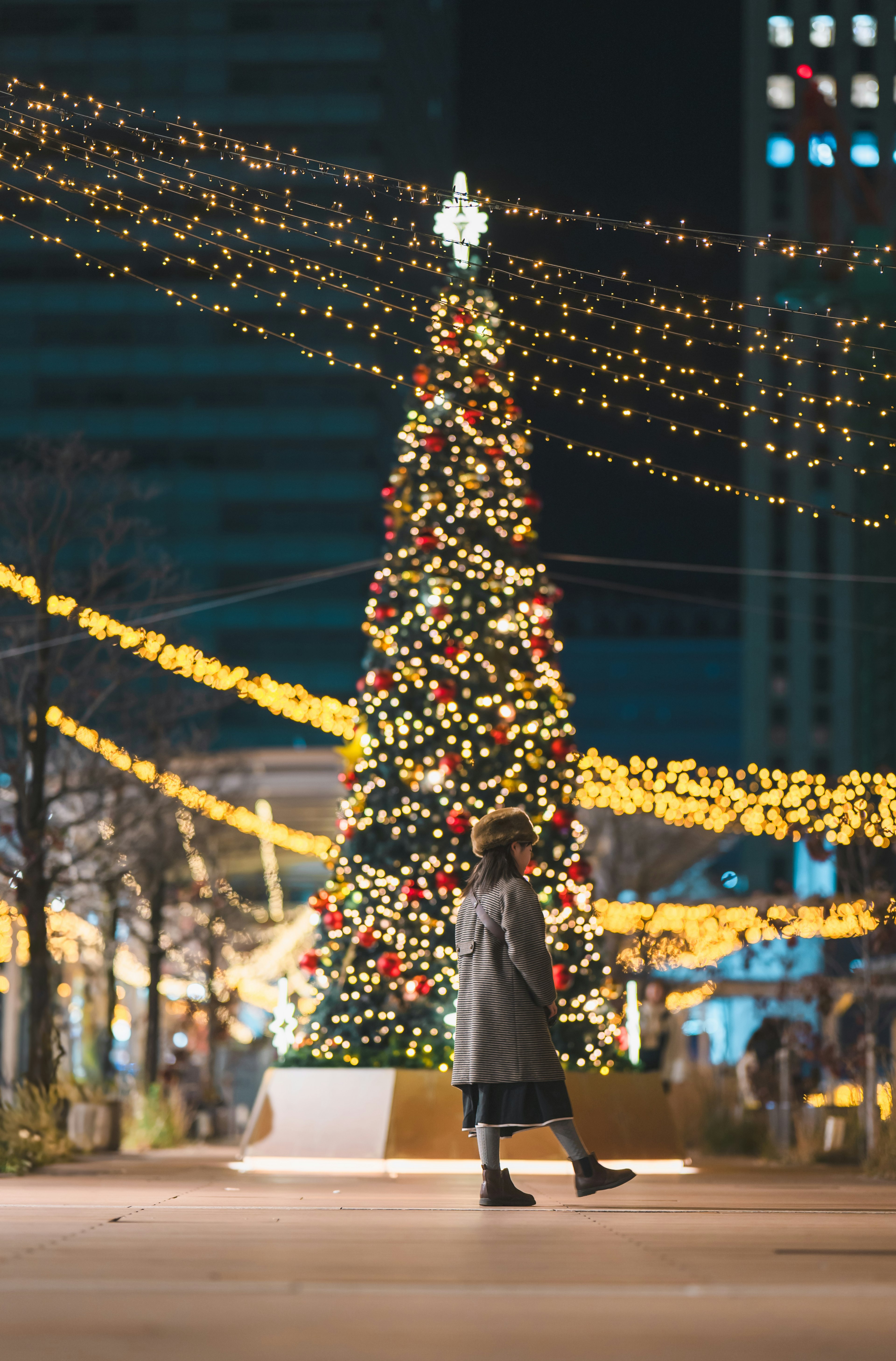 A person walking near a beautifully decorated Christmas tree with festive lights