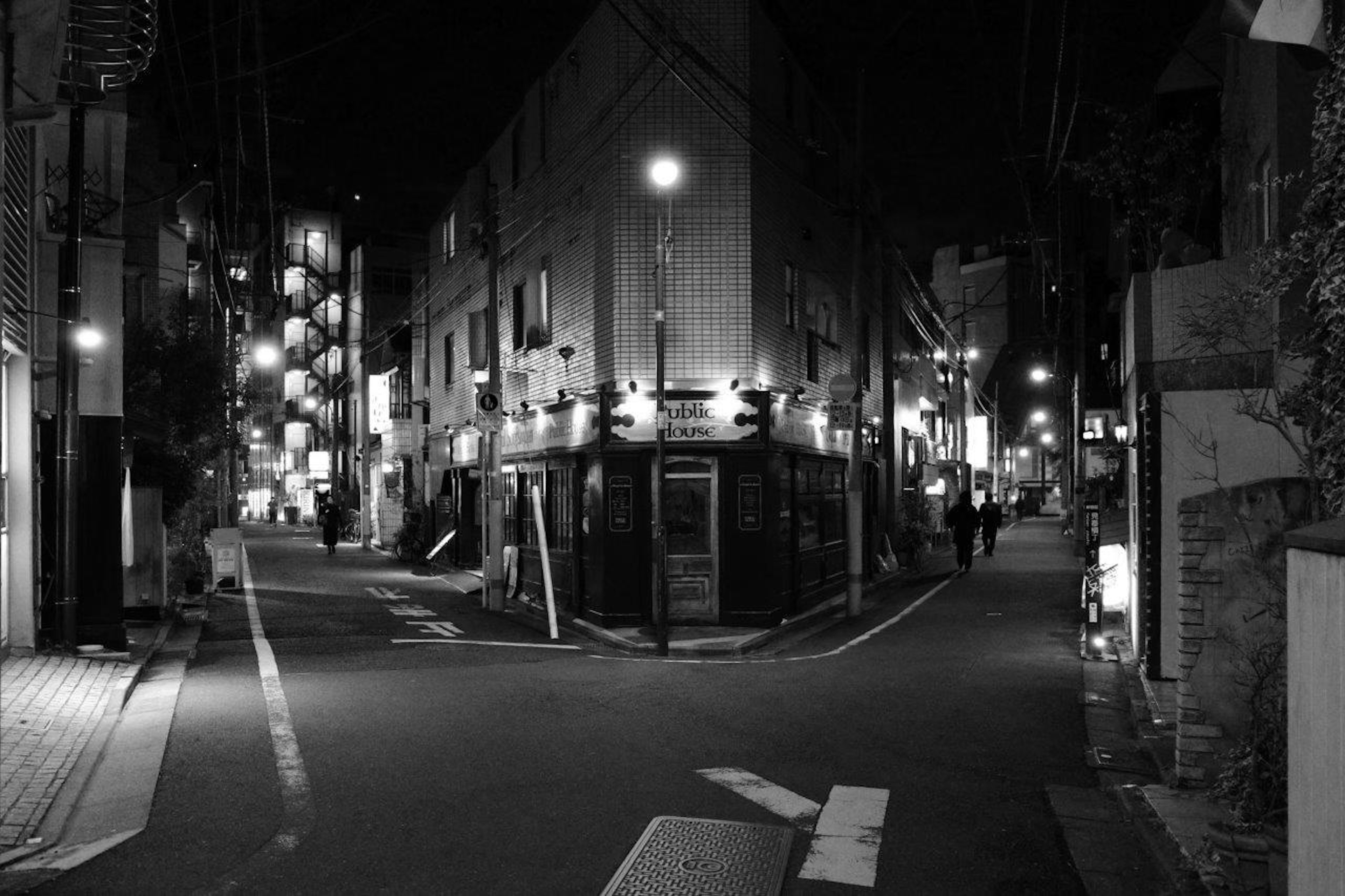 Foto en blanco y negro de una esquina de calle por la noche con edificios débilmente iluminados y caminos