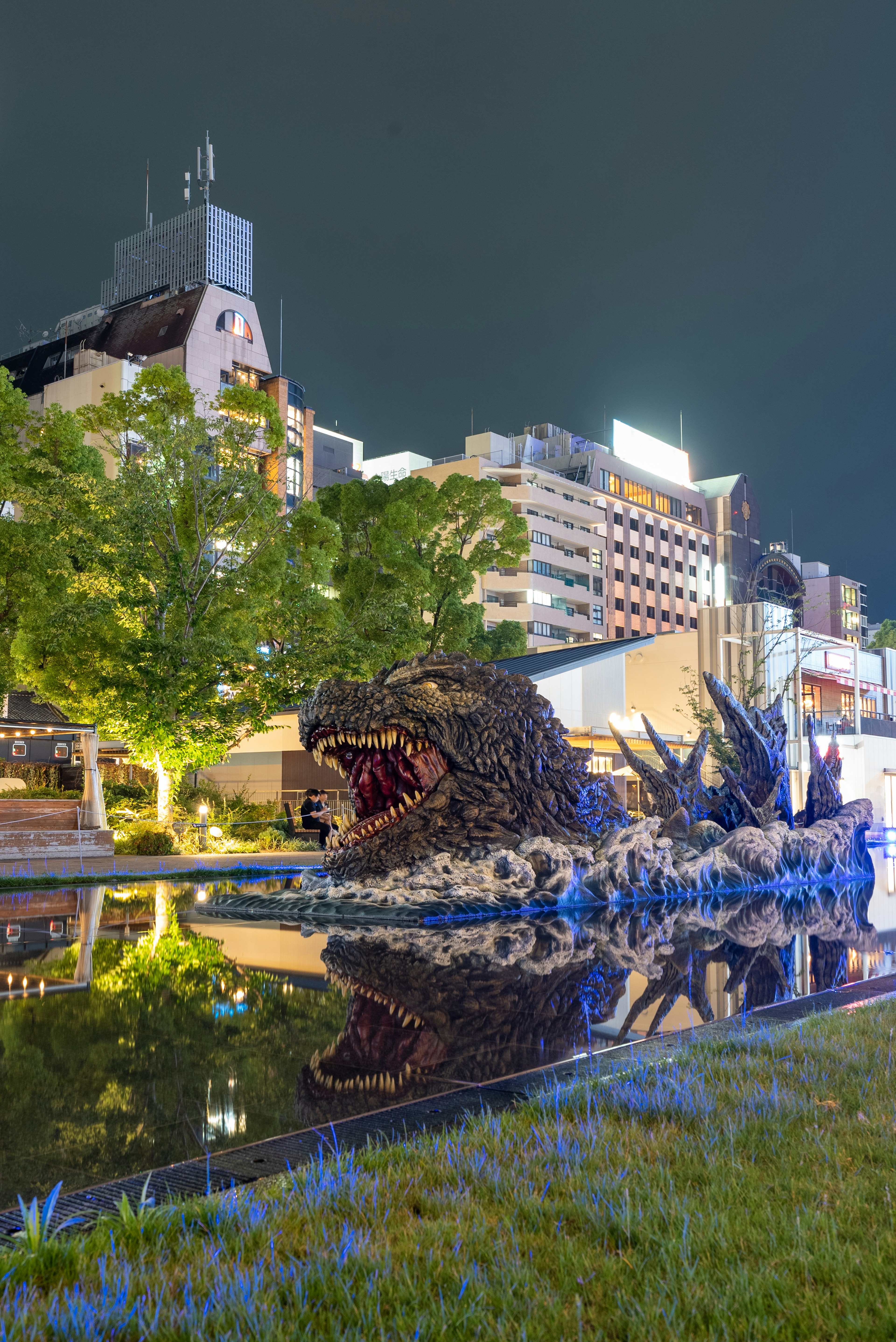 Giant Godzilla statue illuminated at night with reflections in water