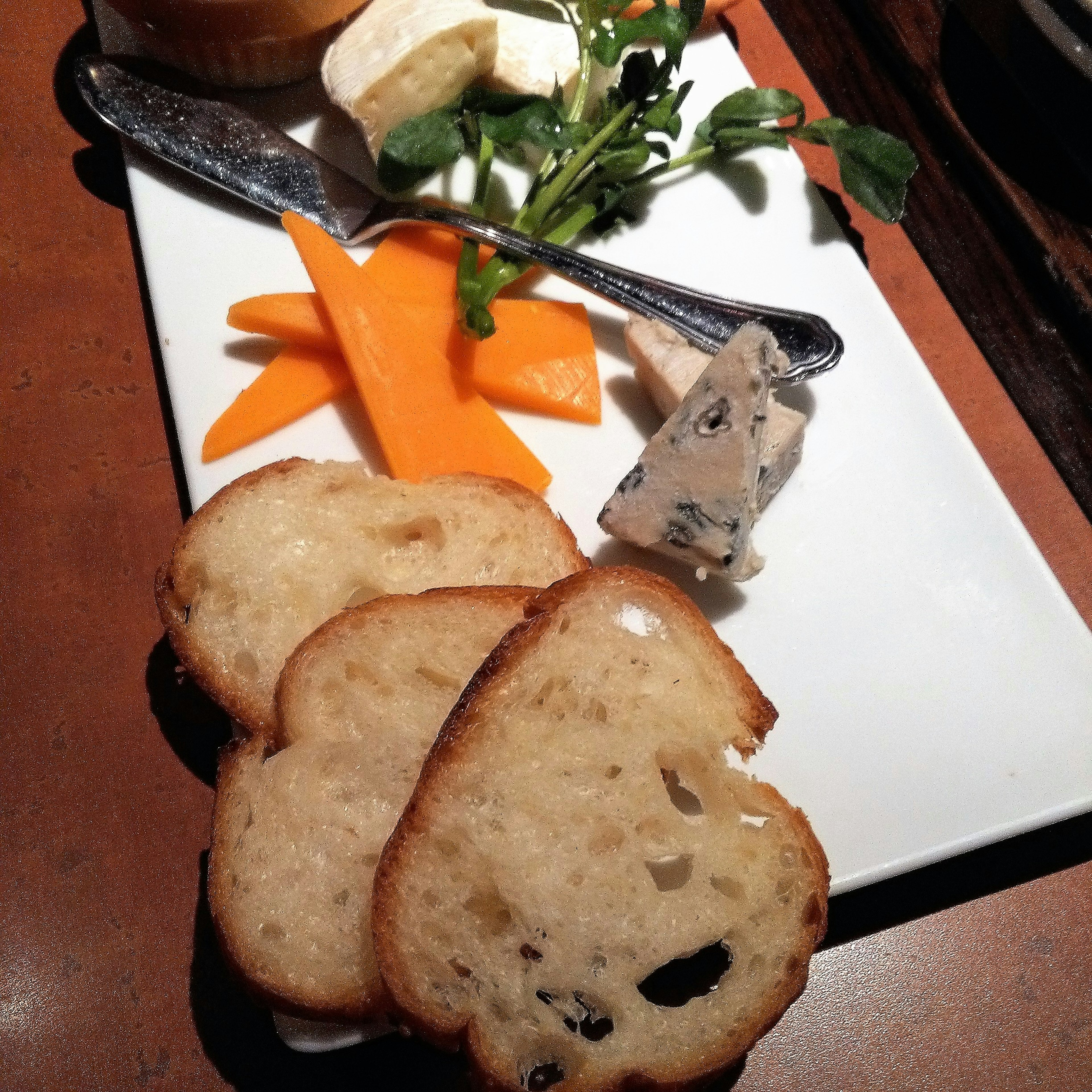 A plate featuring assorted cheeses, sliced bread, and colorful vegetables