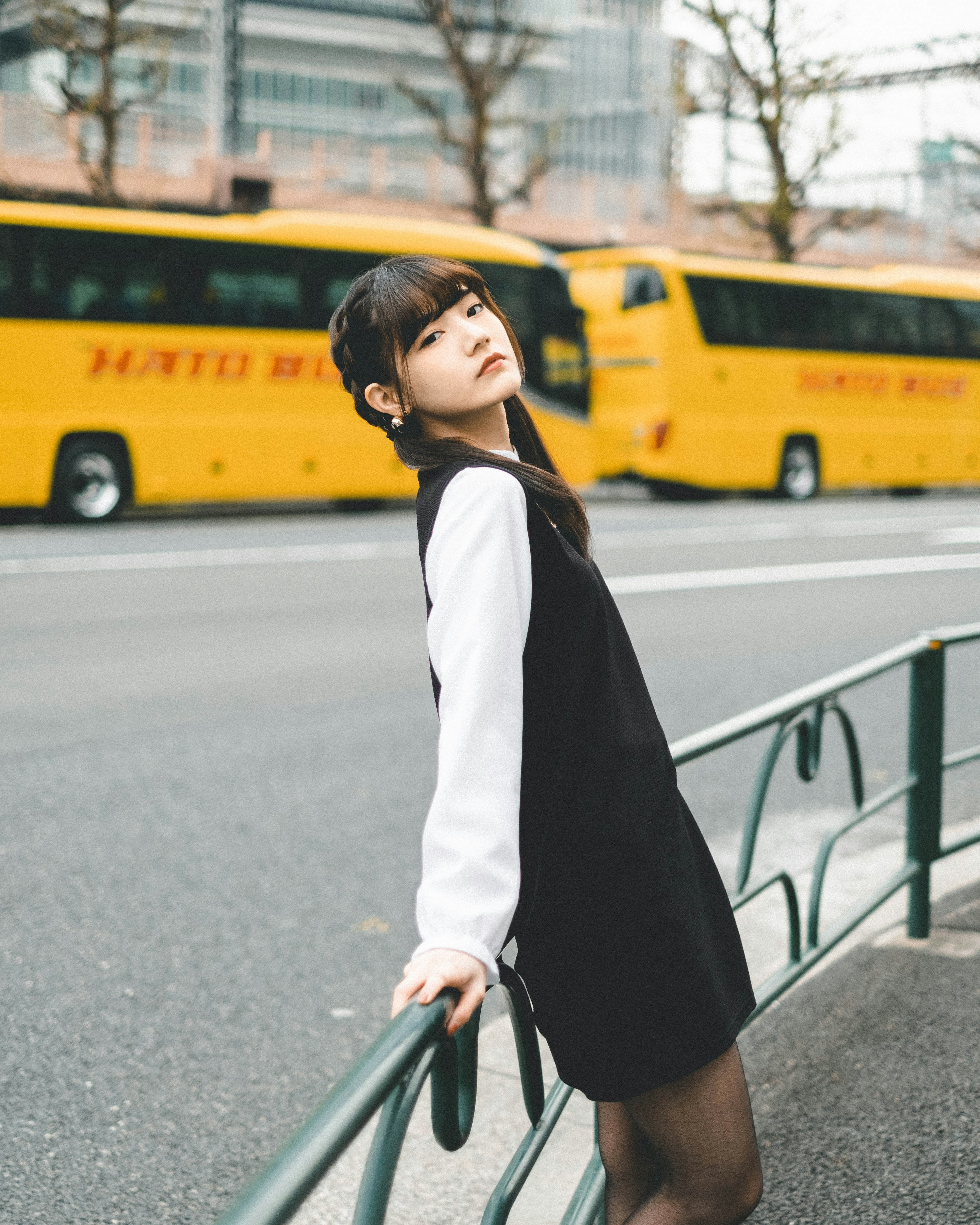 Una mujer con un atuendo negro y blanco posando frente a autobuses amarillos