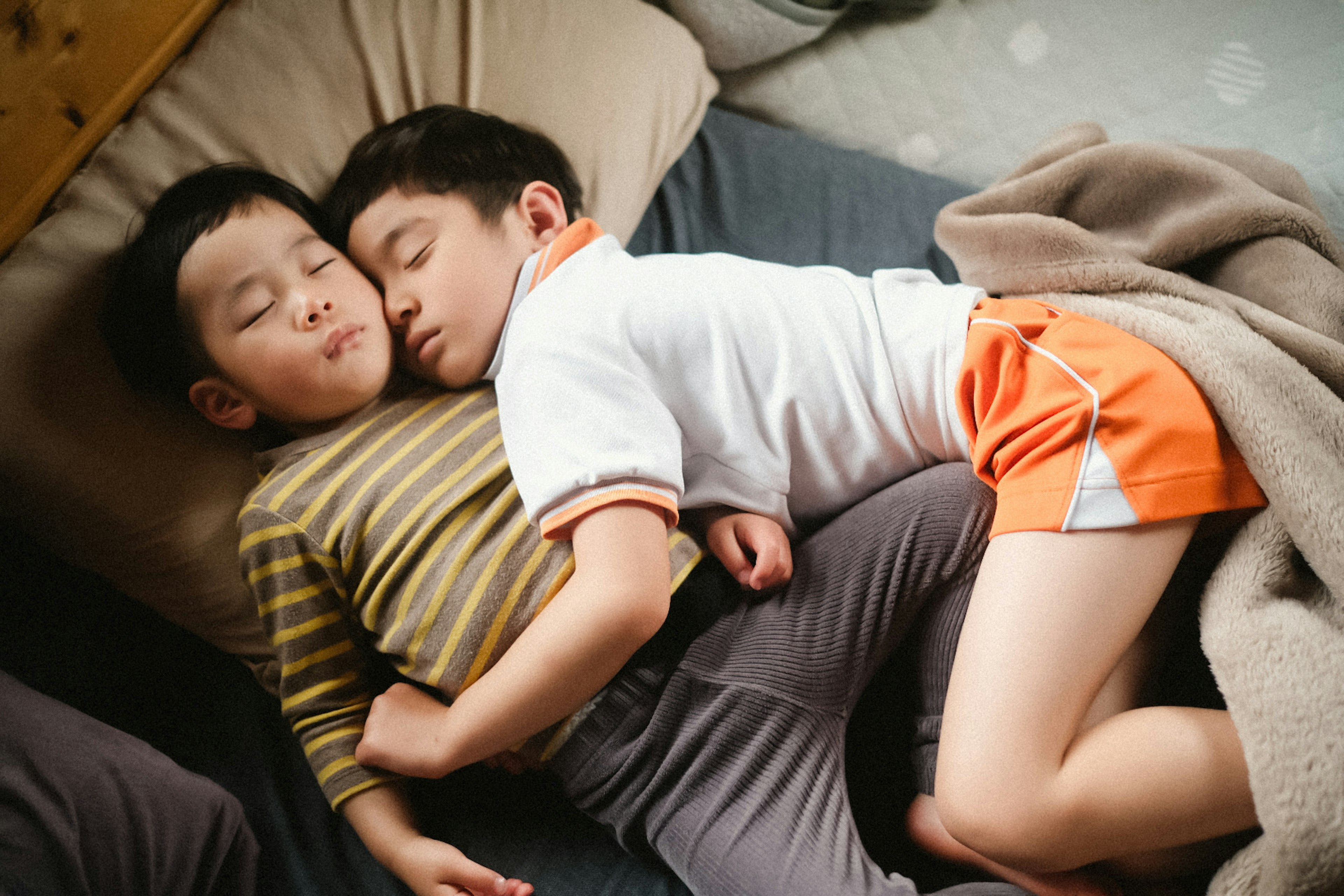 Two boys sleeping together one wearing a striped shirt and the other in a white shirt cuddling