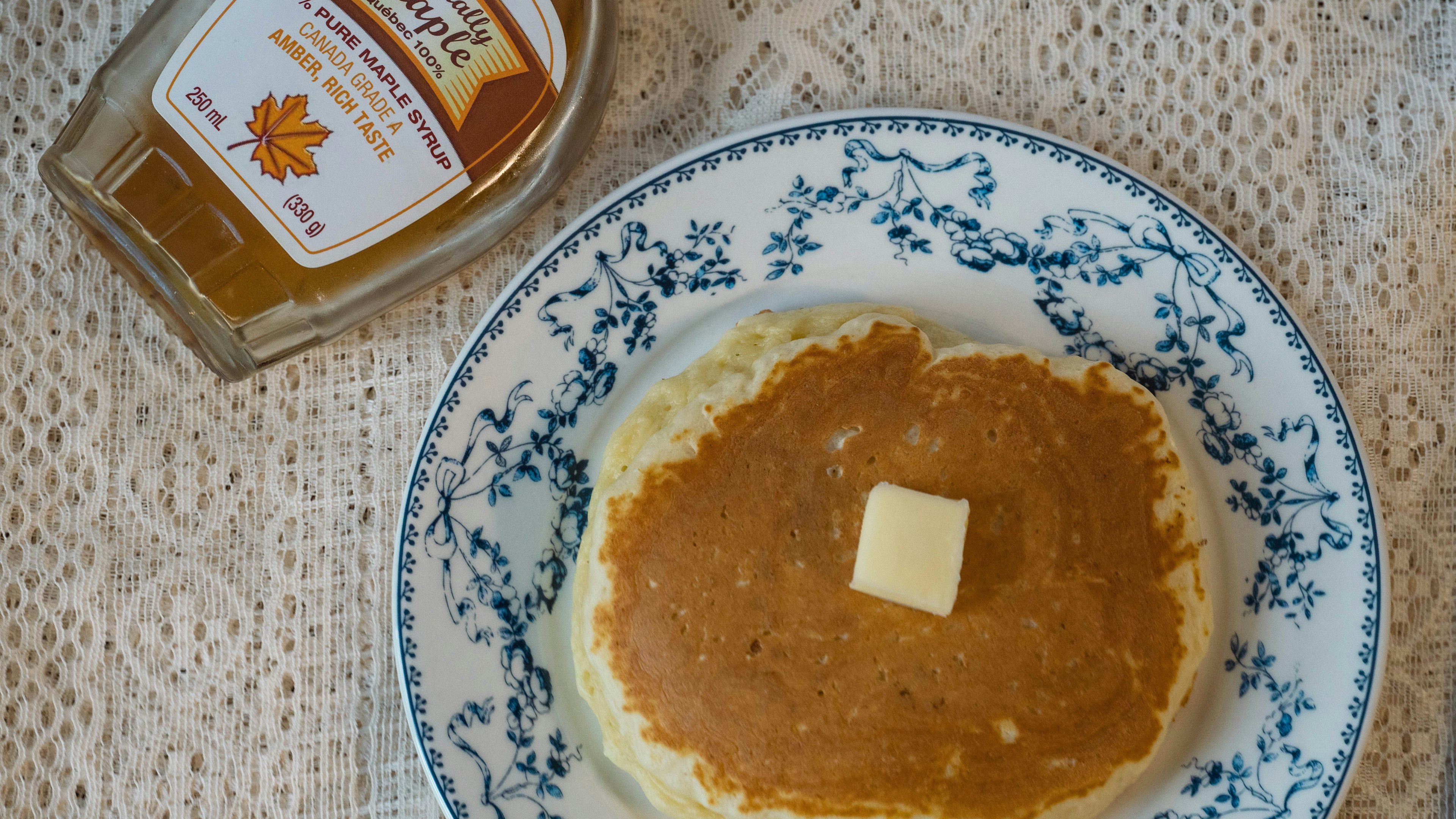 Pancake with butter on a decorative plate and a bottle of maple syrup