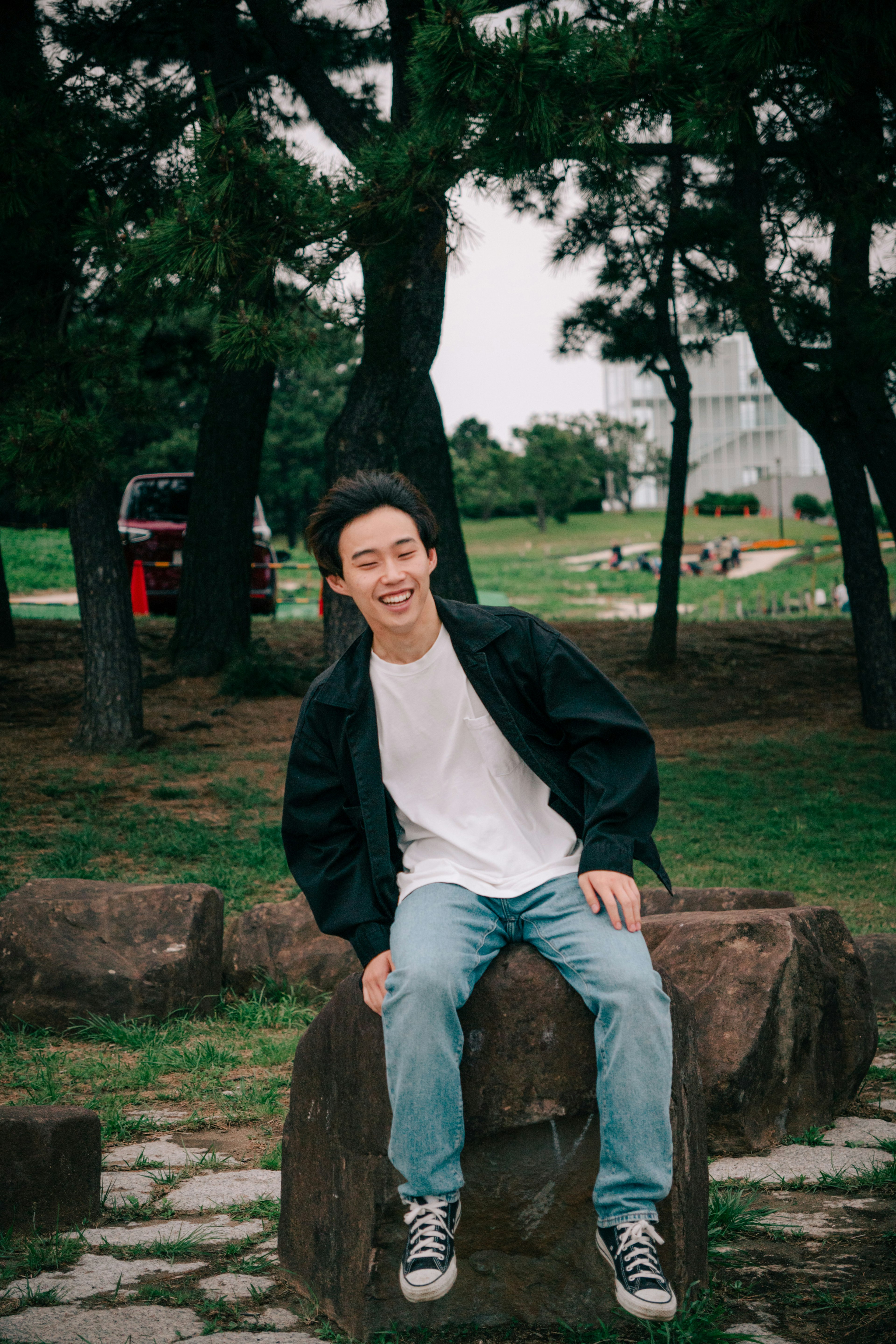 Joven sentado en una piedra en un parque sonriendo con ropa casual