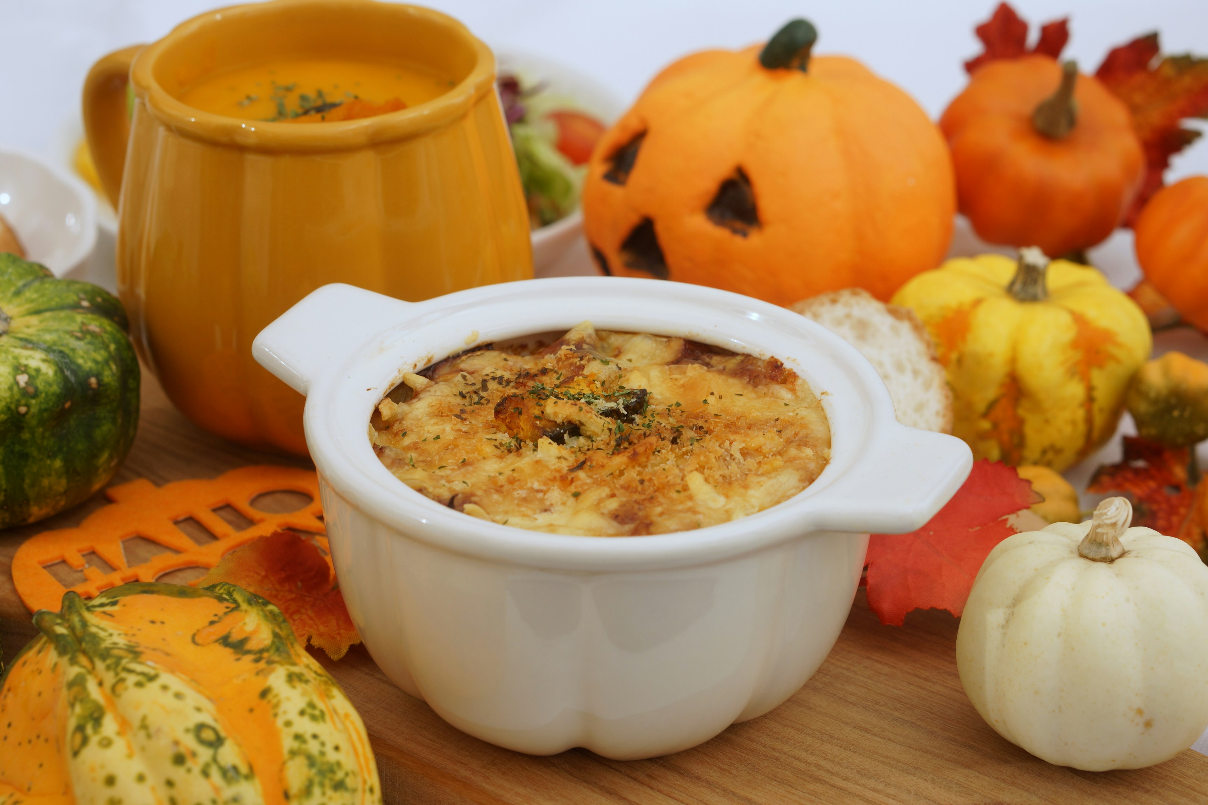 Baked dish in a white bowl surrounded by small pumpkins and autumn decorations