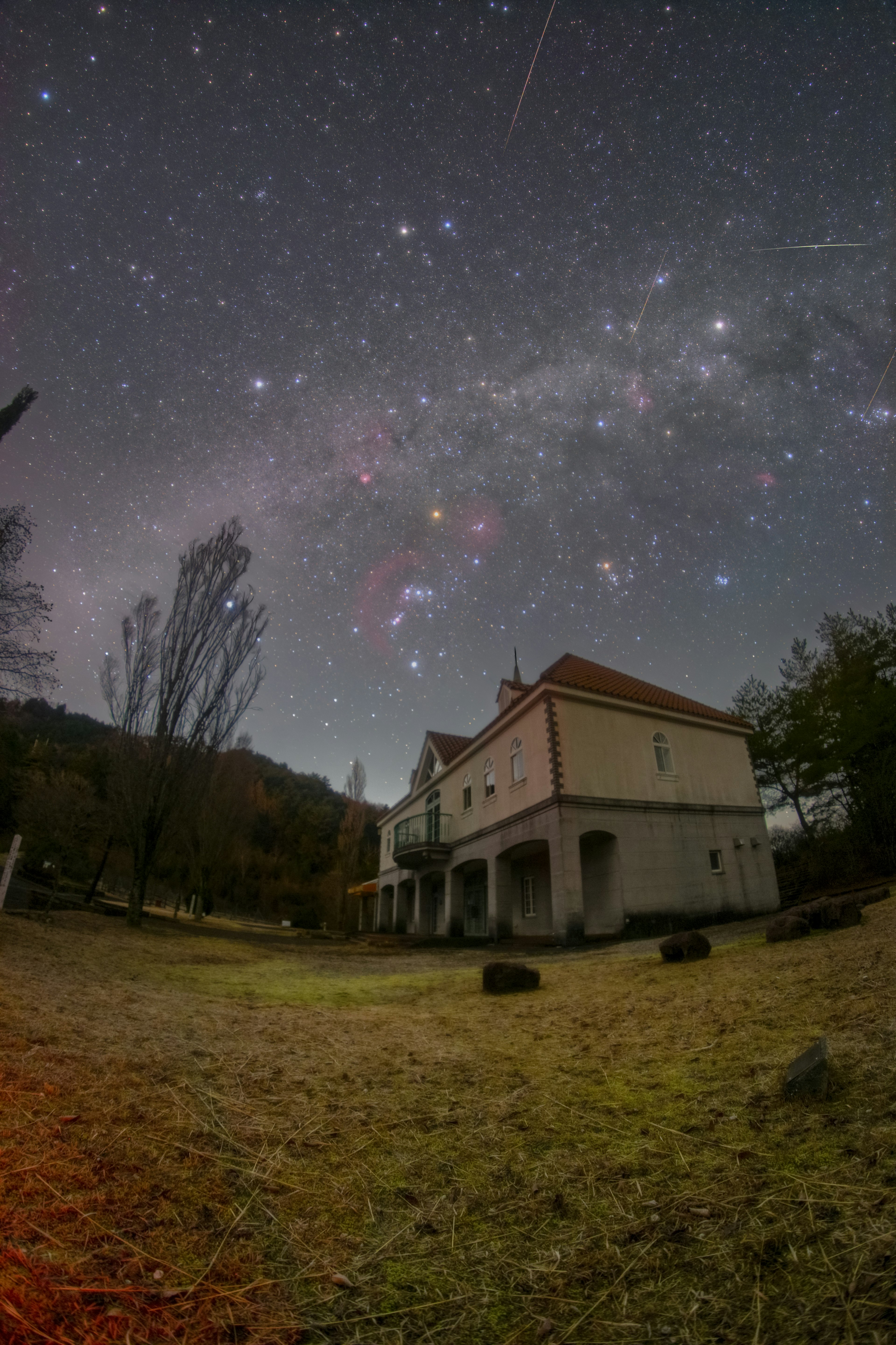 夜空に広がる星々と流れ星の下に立つ古い家