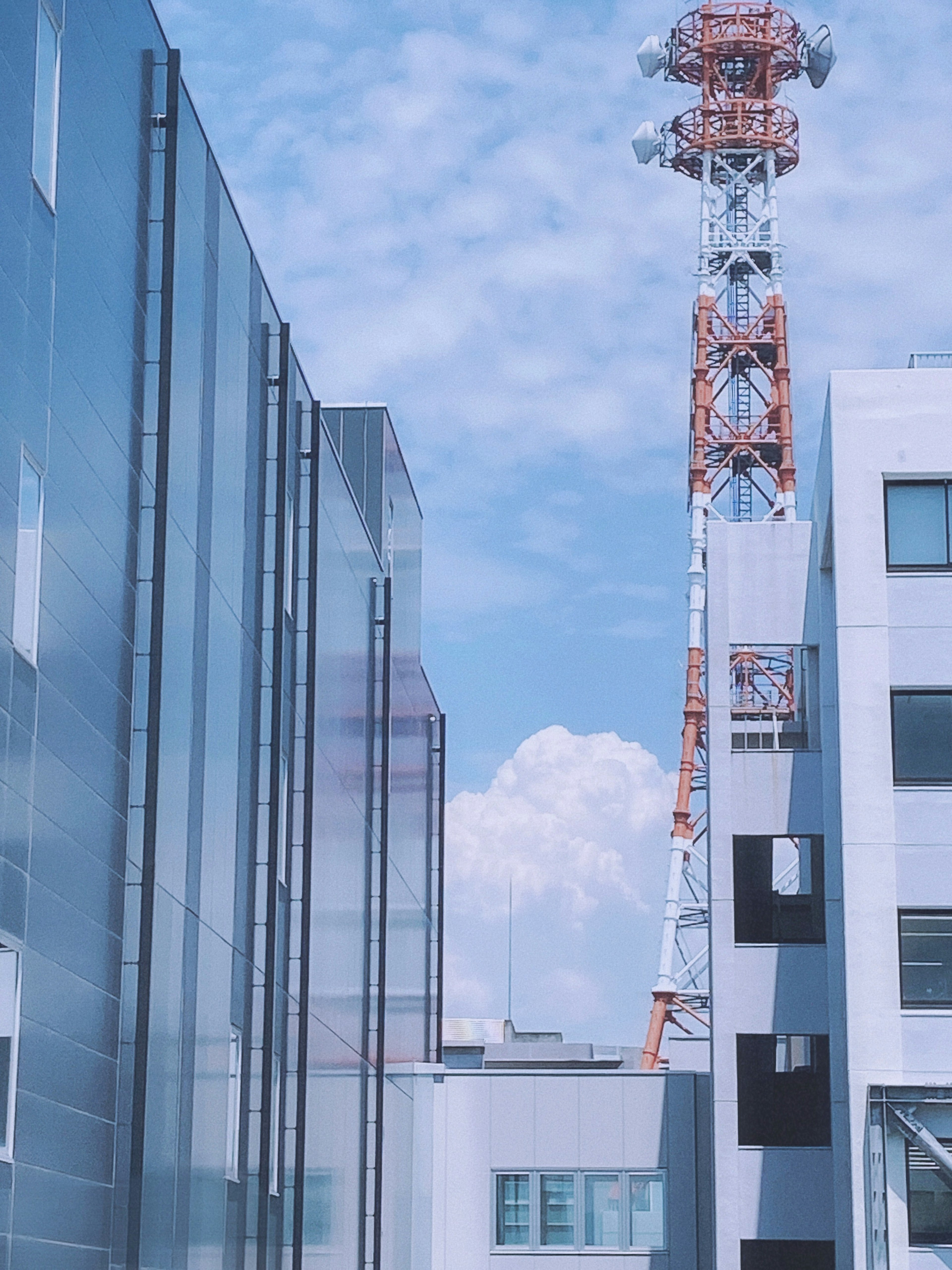 现代建筑下方有高通信塔，天空湛蓝，云朵飘浮