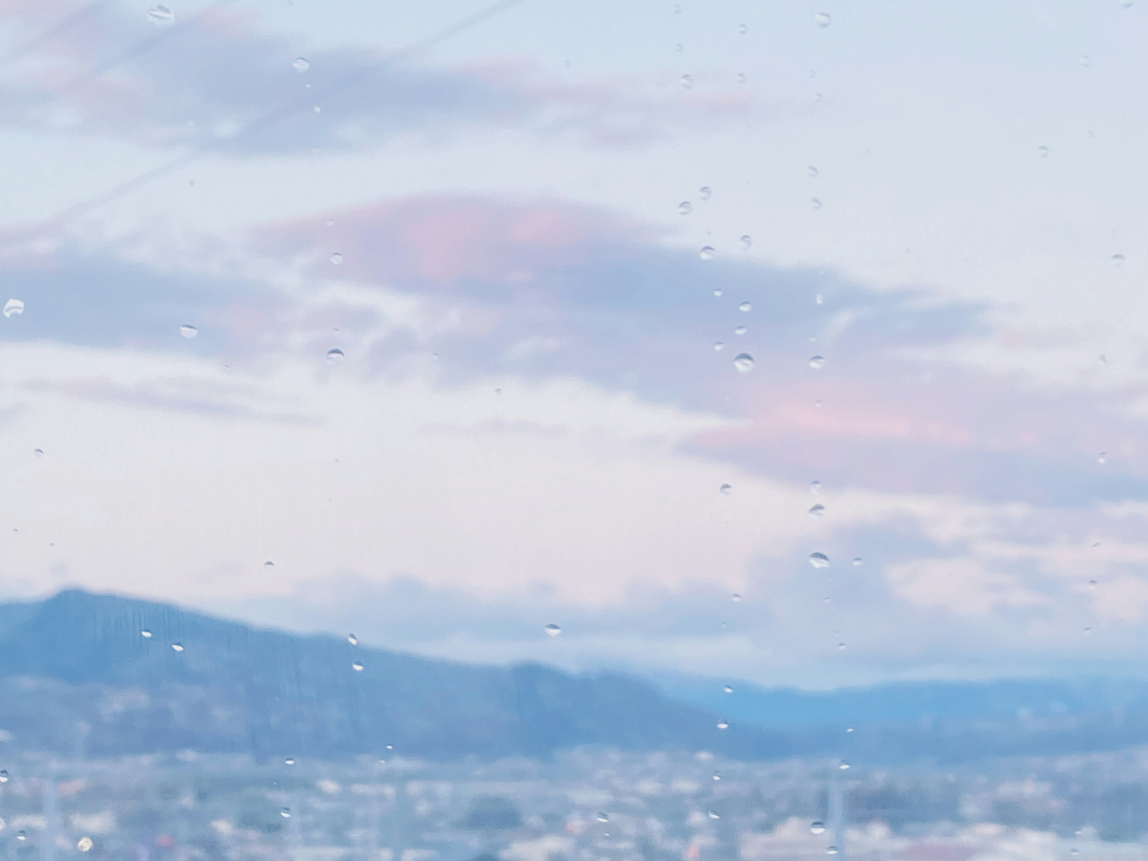 View of blue mountains and soft-colored sky through raindrop-covered window