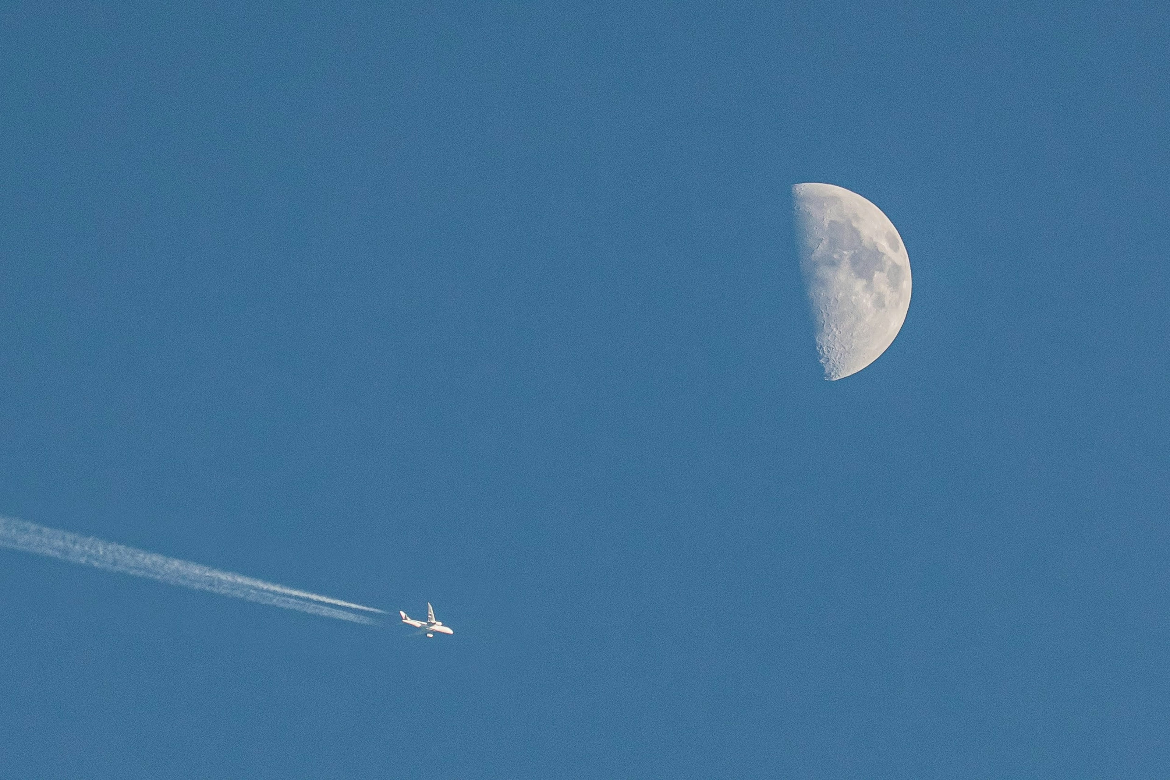 Halbmond im blauen Himmel mit Flugzeugkondensstreifen