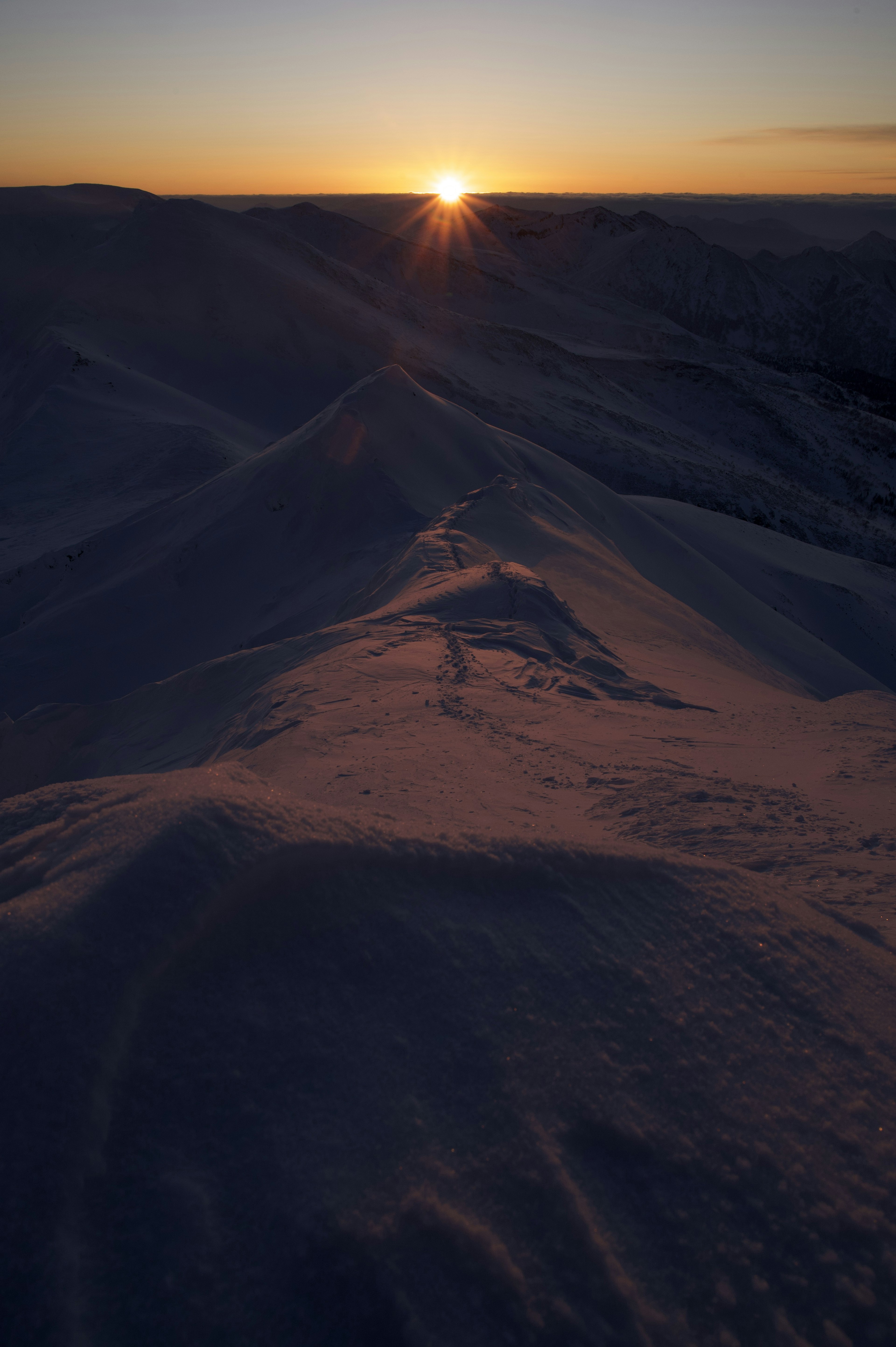 Amanecer sobre colinas nevadas con sombras y luz suave