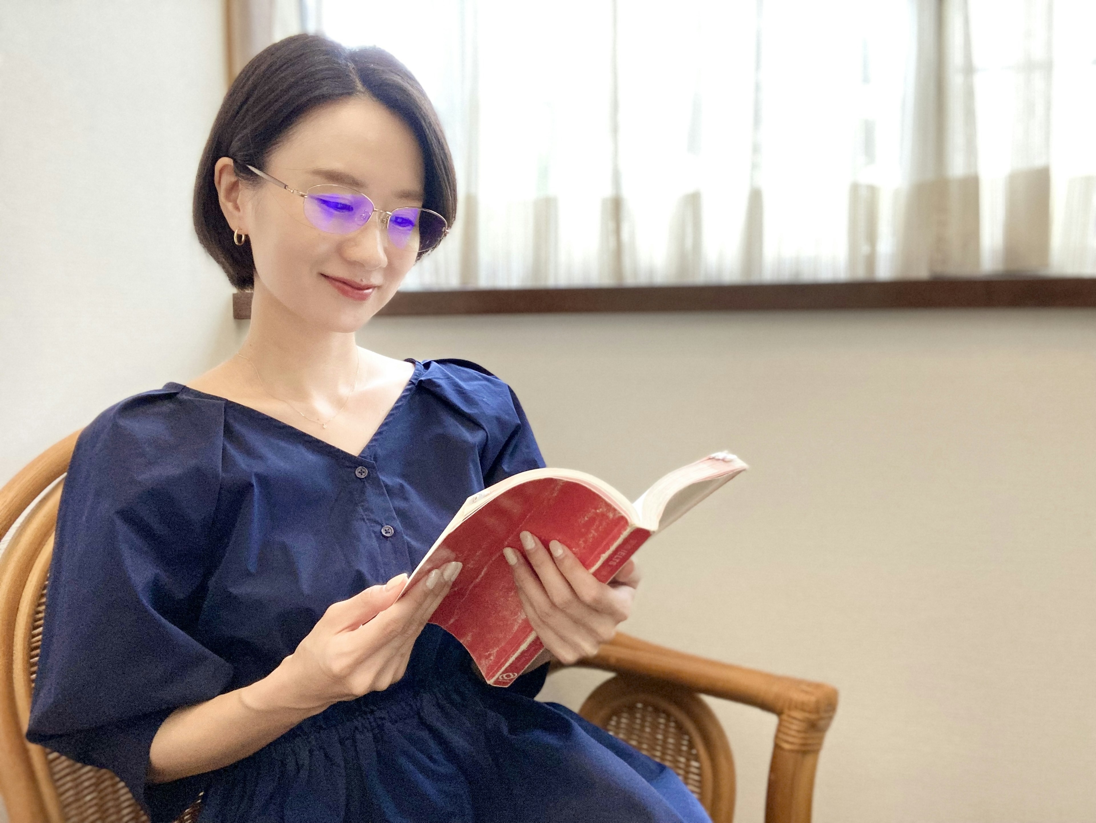 Woman with blue glasses reading a book while sitting in a chair