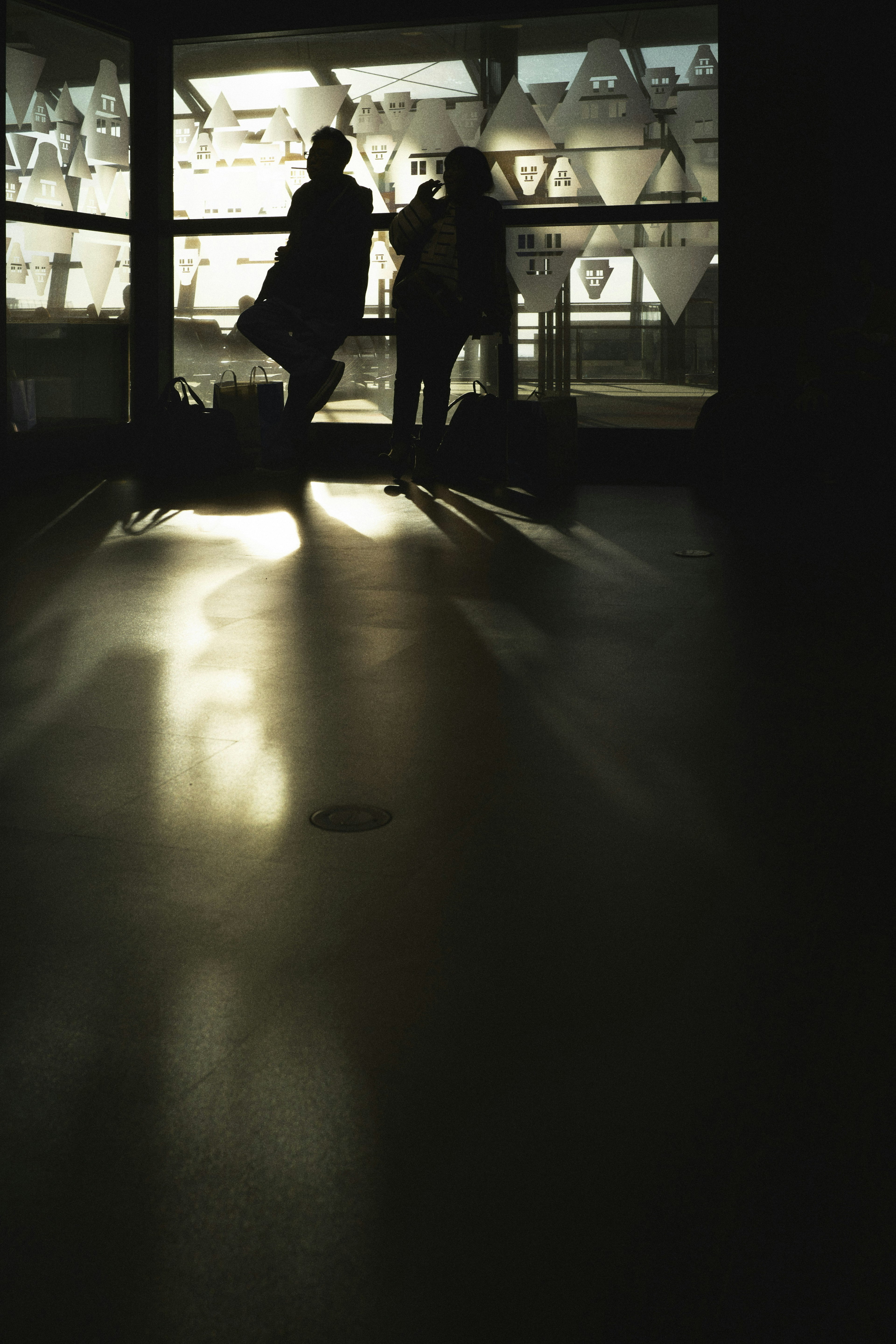 Silhouettes de deux personnes debout près d'une fenêtre avec des reflets de lumière