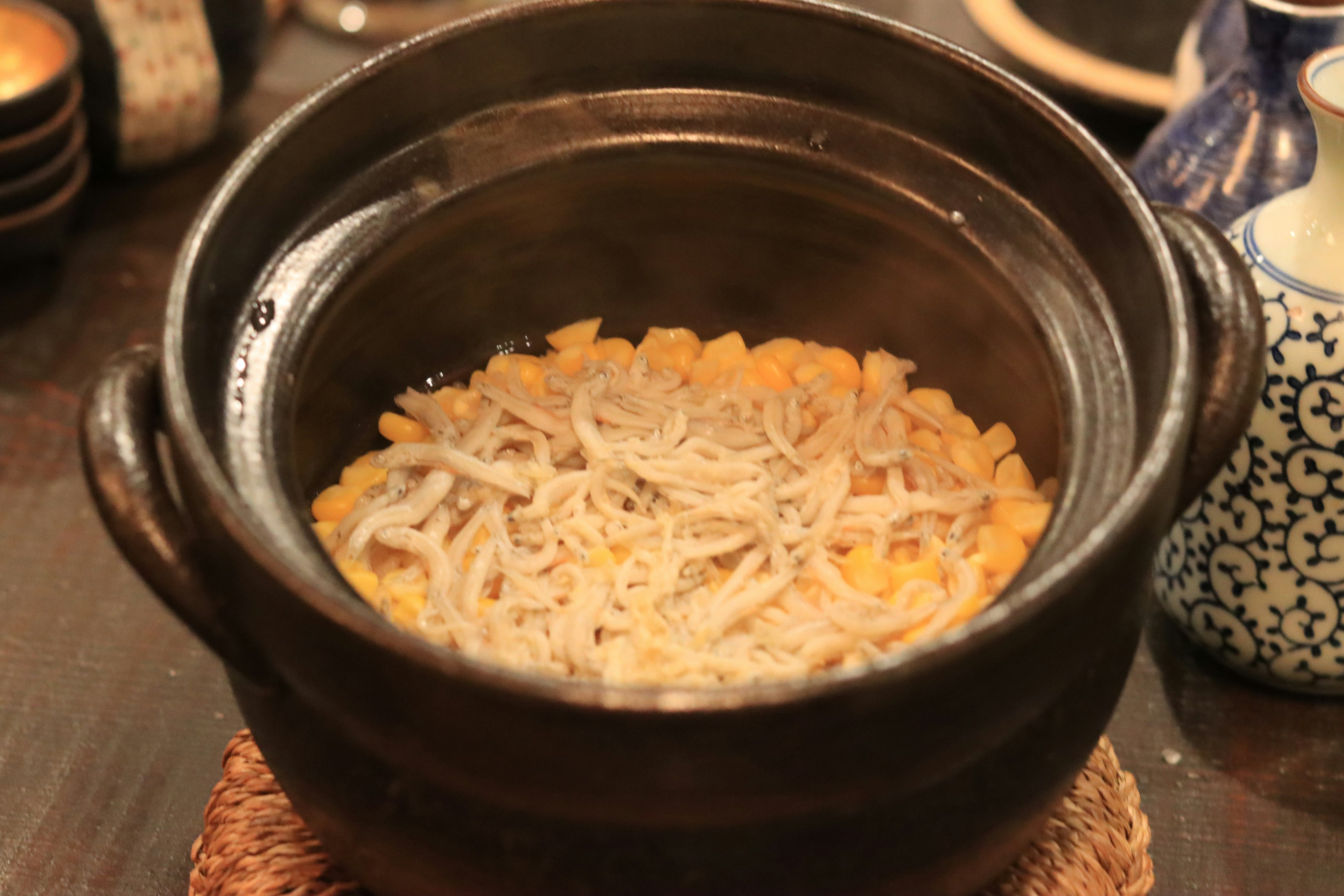 Clay pot filled with rice topped with small fish and ginger