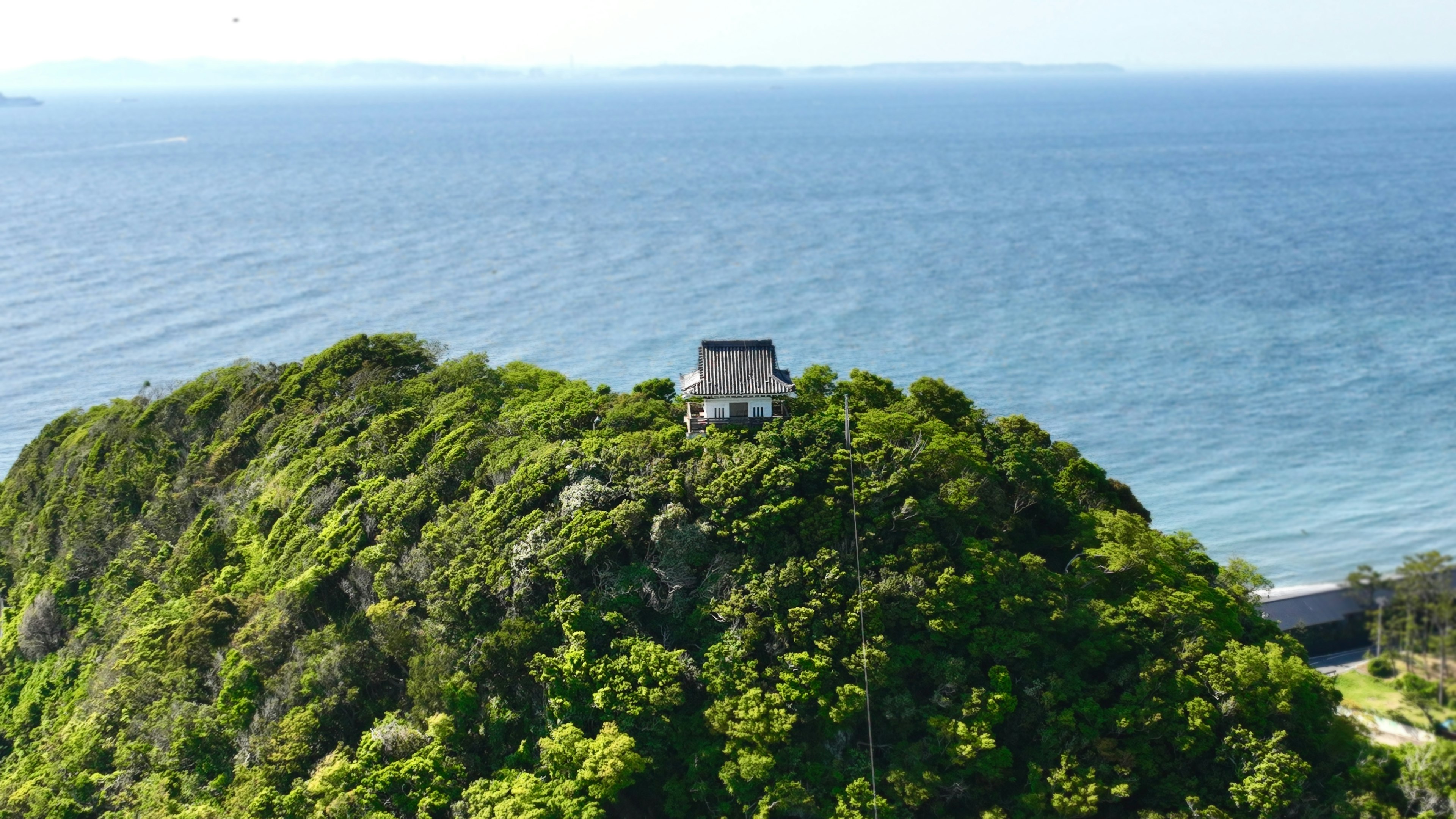 一座小建筑坐落在俯瞰大海的山丘上，周围环绕着郁郁葱葱的绿树