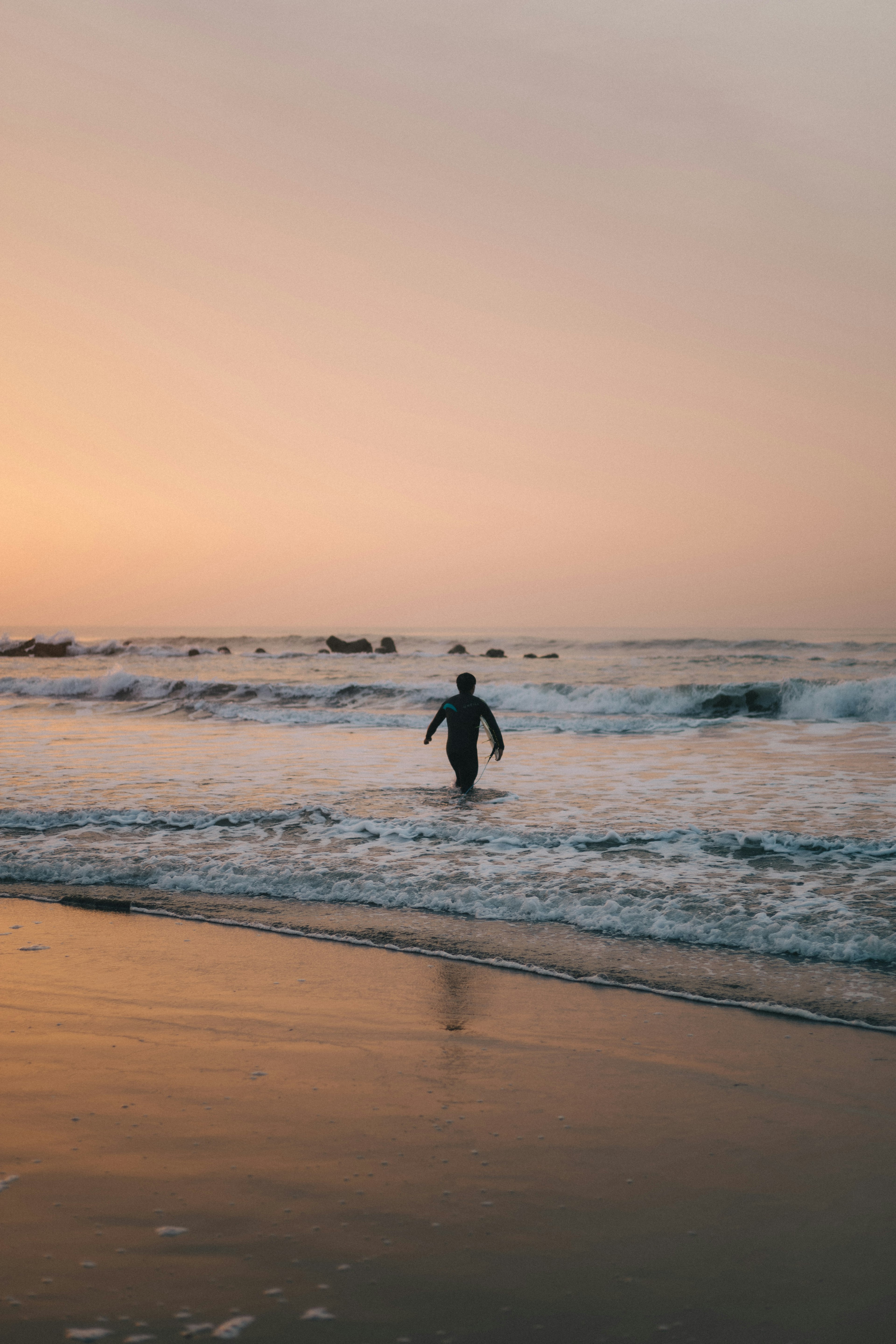 夕焼けの海で波の中を歩く人のシルエット