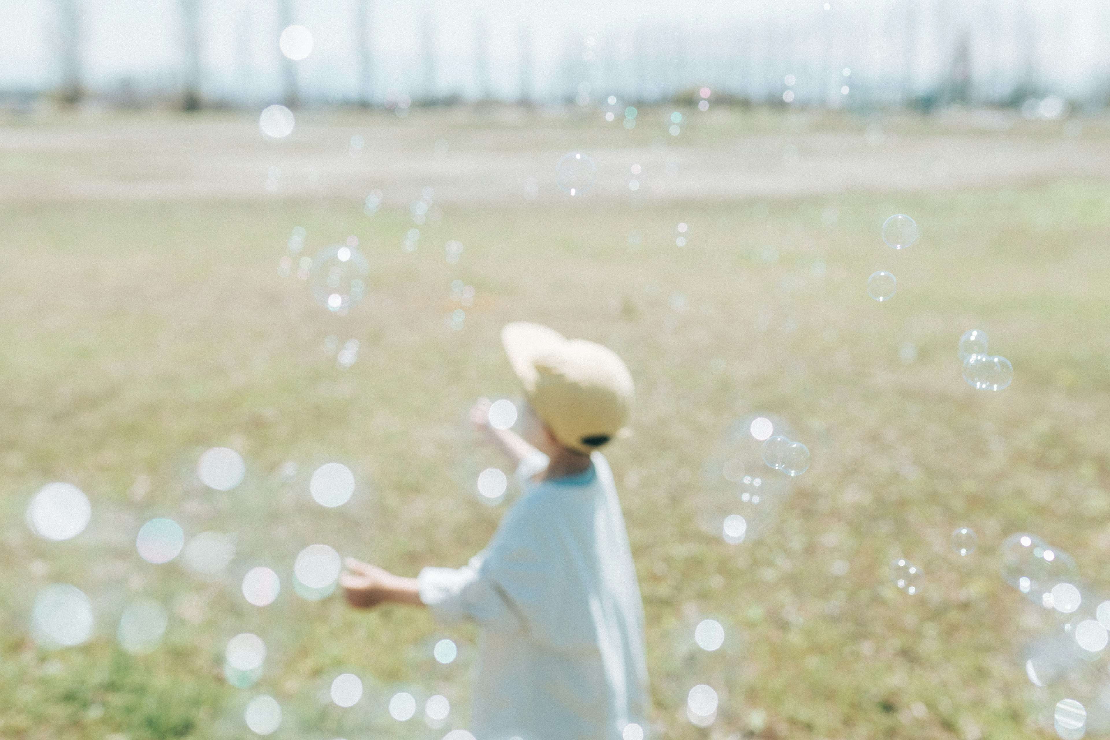 Child chasing bubbles in a sunny field with a light background