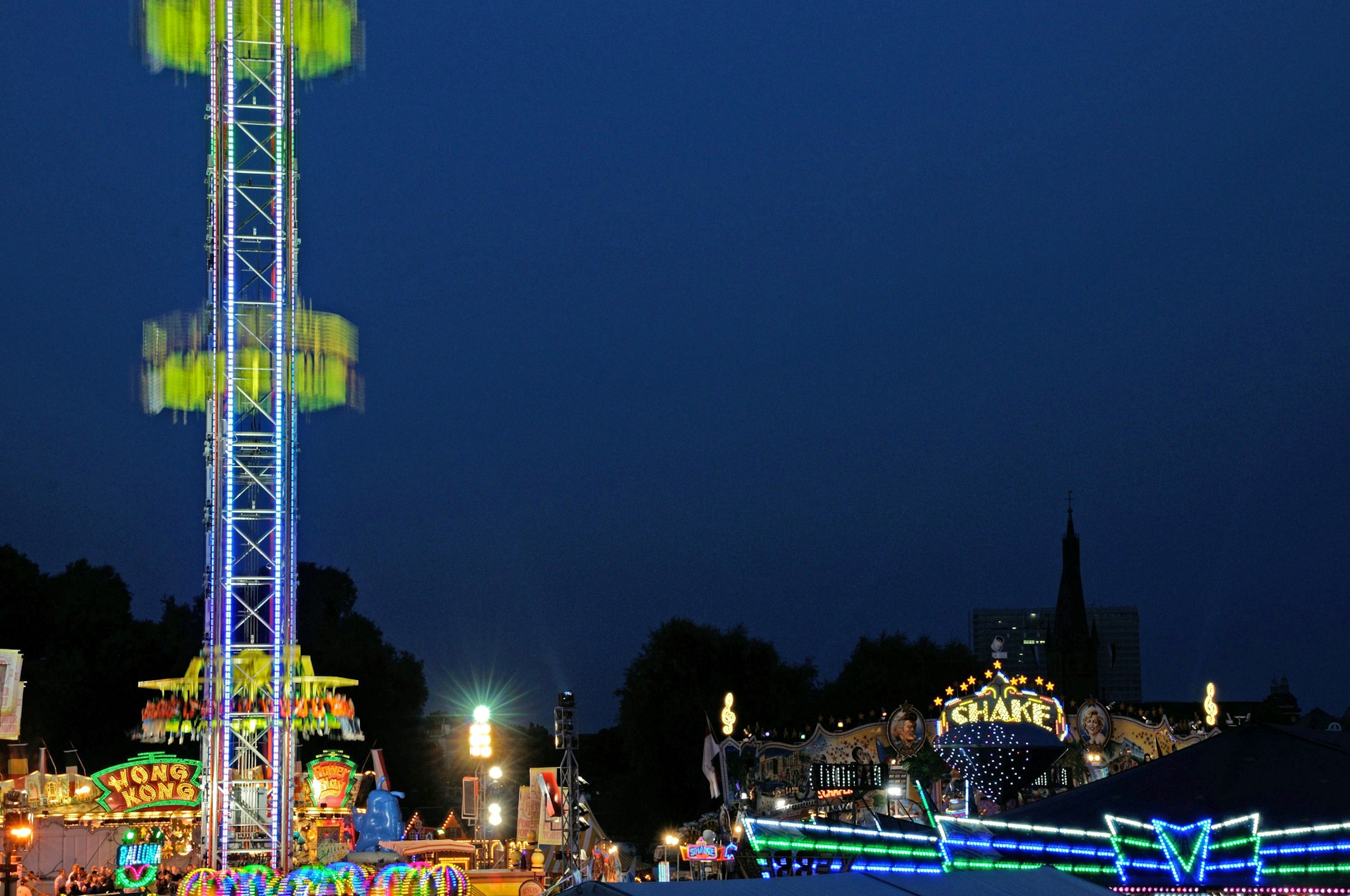 Nachtaufnahme eines Vergnügungsparks mit einem hellen Riesenrad und bunten Fahrgeschäften