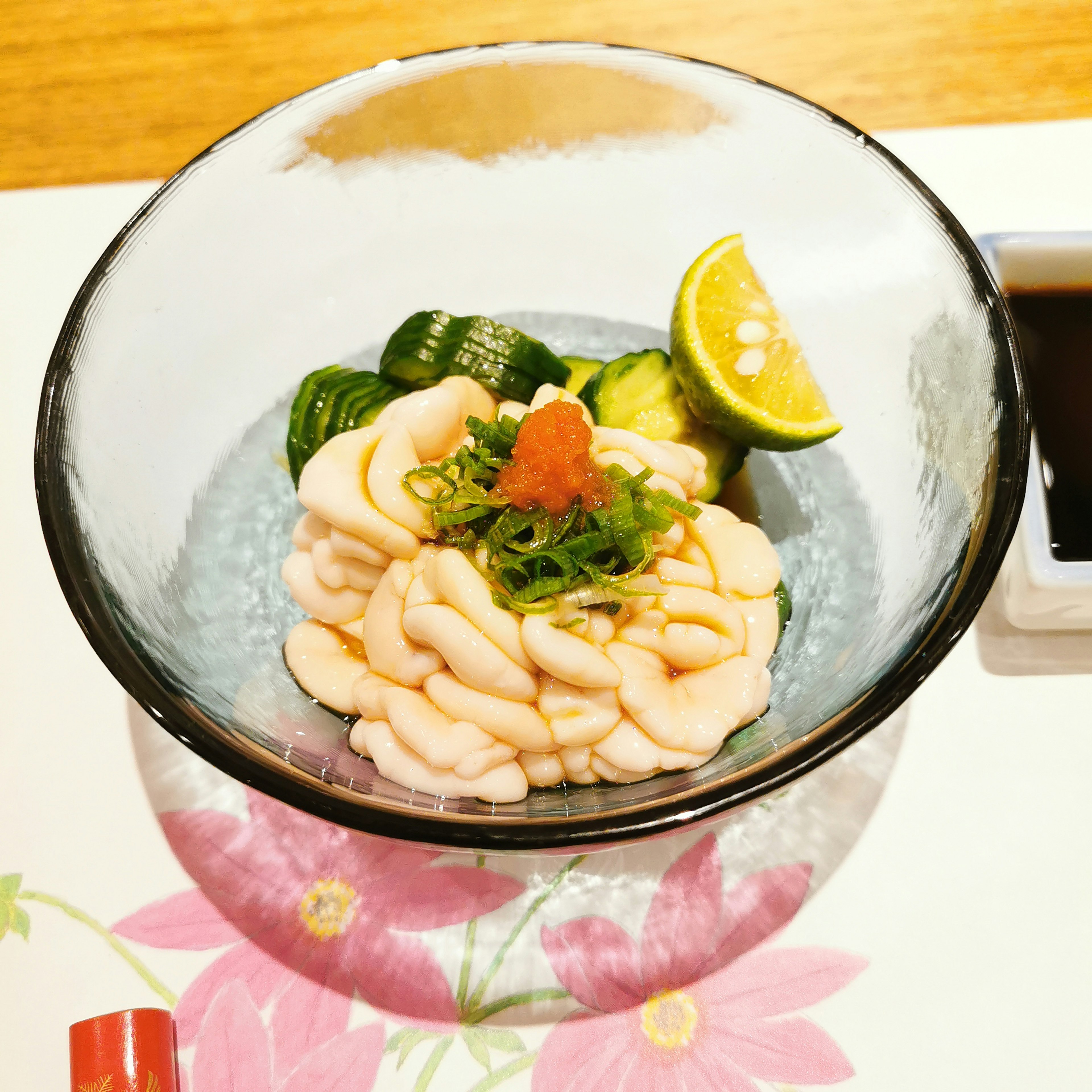 A beautifully arranged sashimi in a glass bowl with cucumber slices and lime wedges