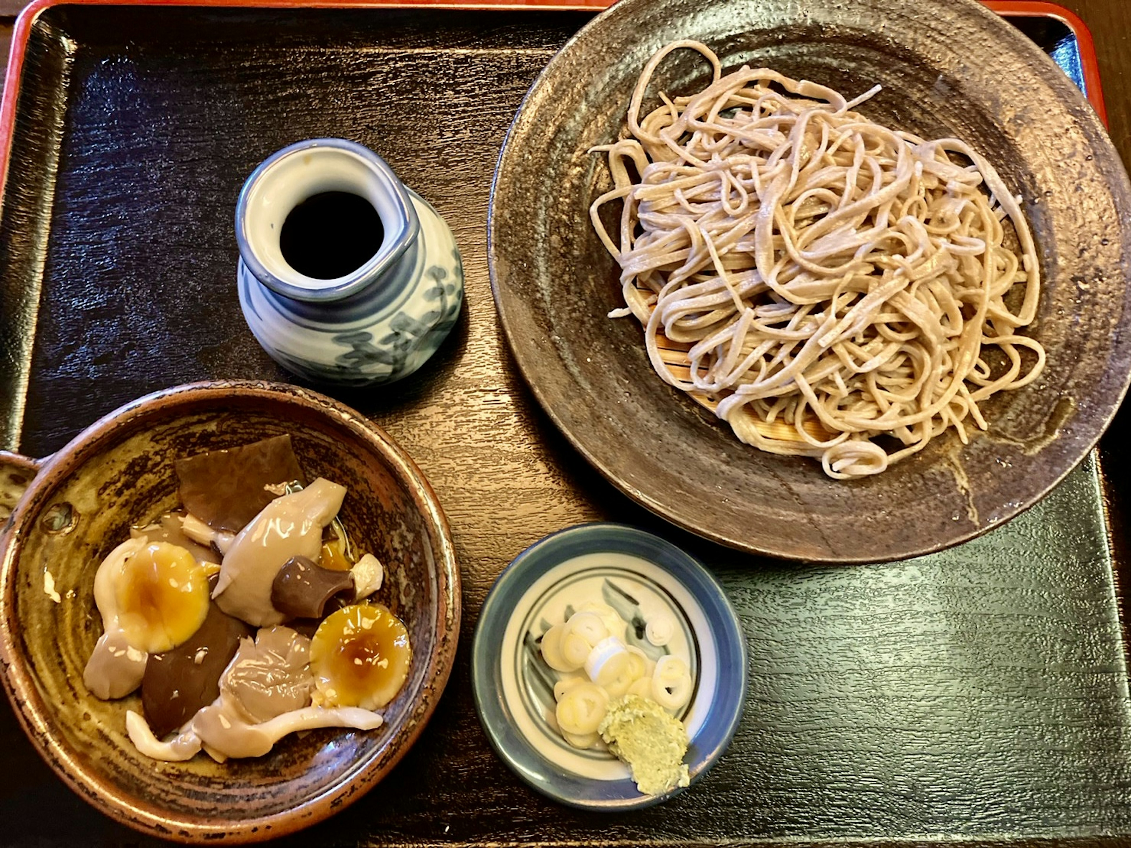 Un plato de fideos soba servido con un acompañamiento de cerdo y salsa para mojar