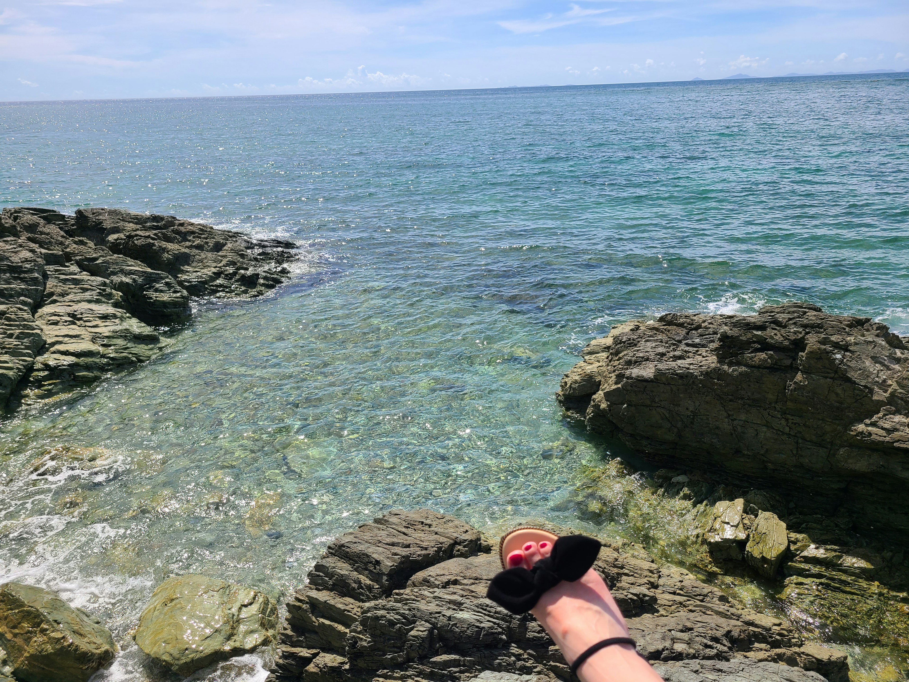 A view of rocky shoreline with a hand reaching towards the ocean and waves