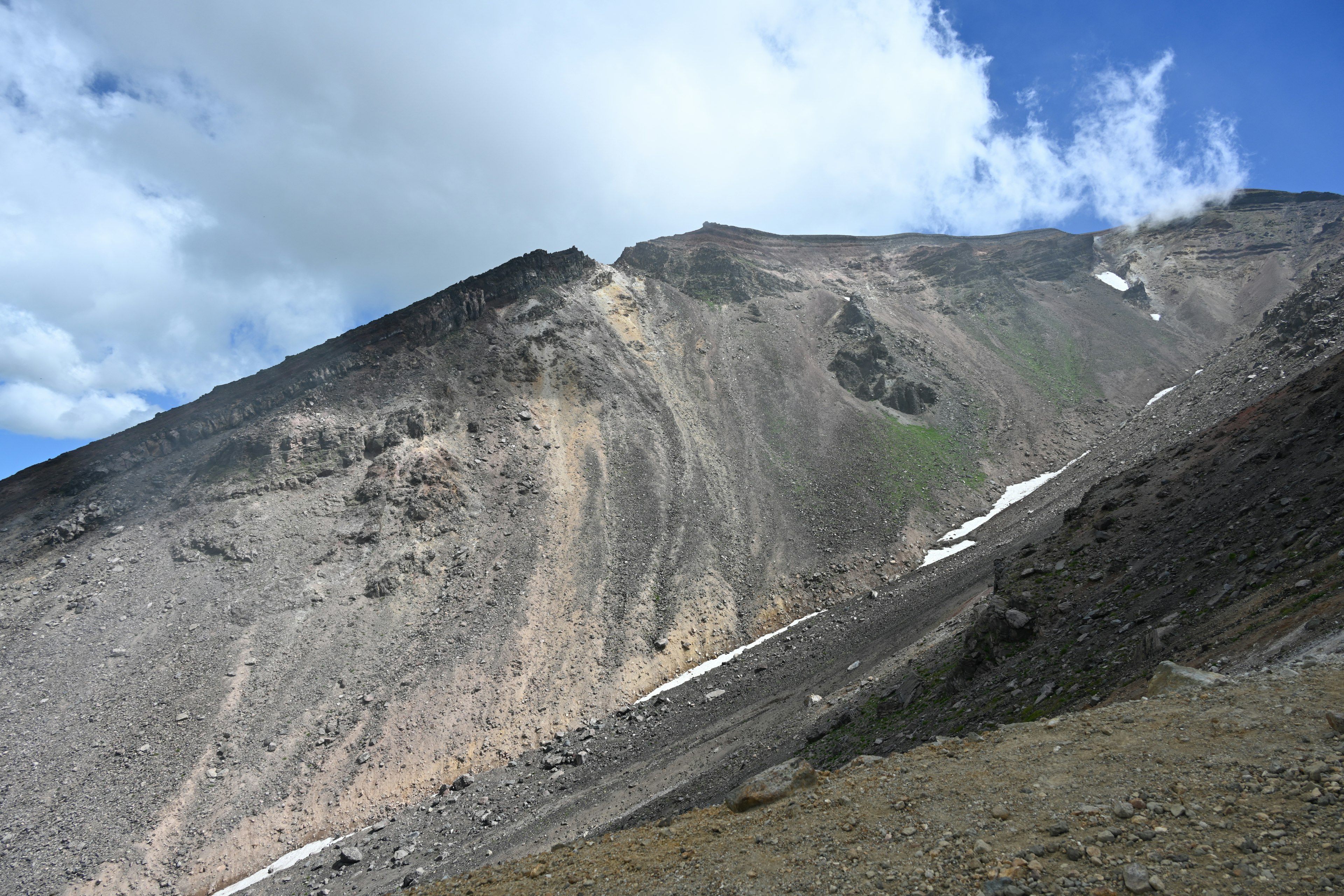 Steiler Berghang unter einem blauen Himmel mit Wolken