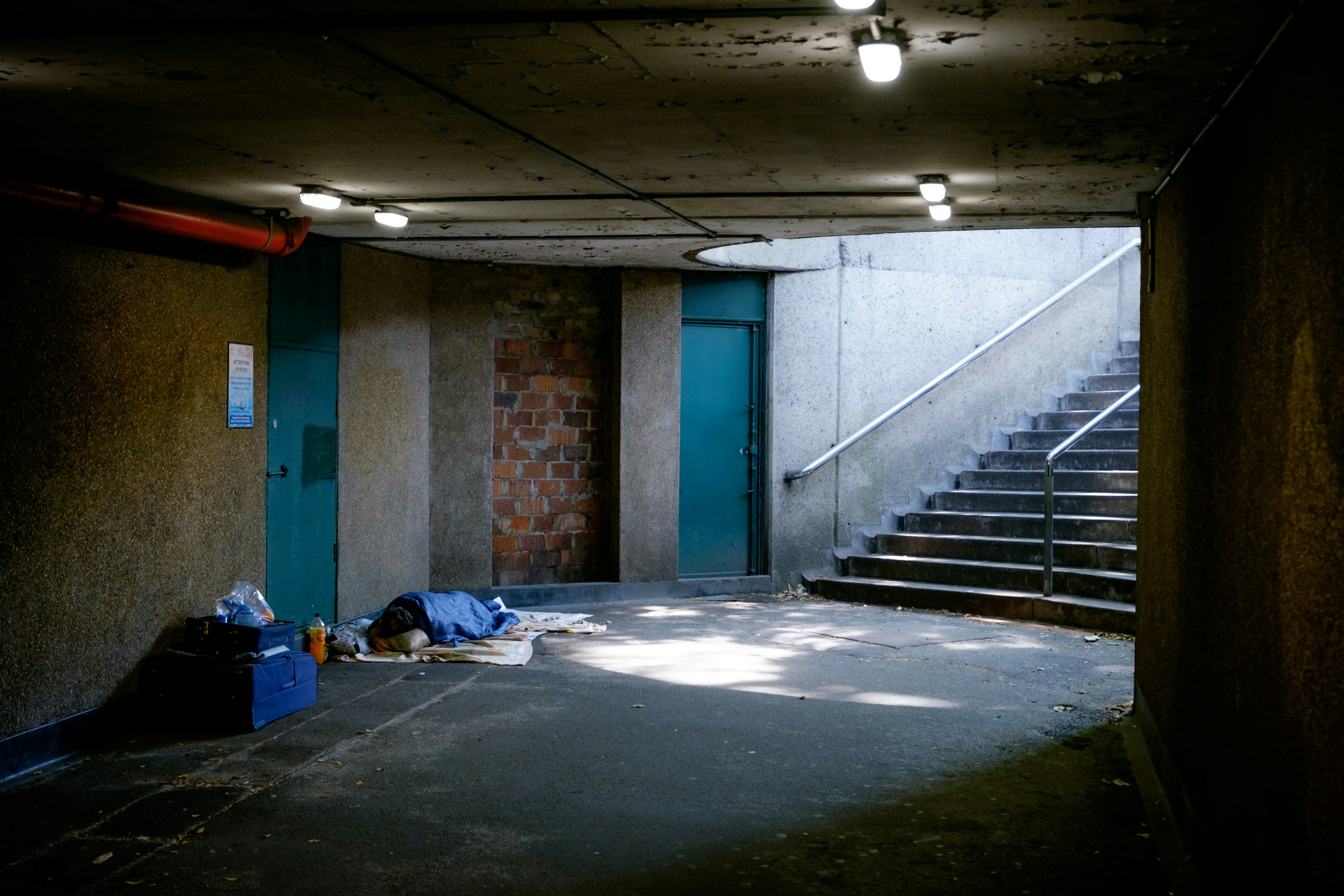 Passage faiblement éclairé avec une couverture bleue au sol escaliers et une porte bleue visible