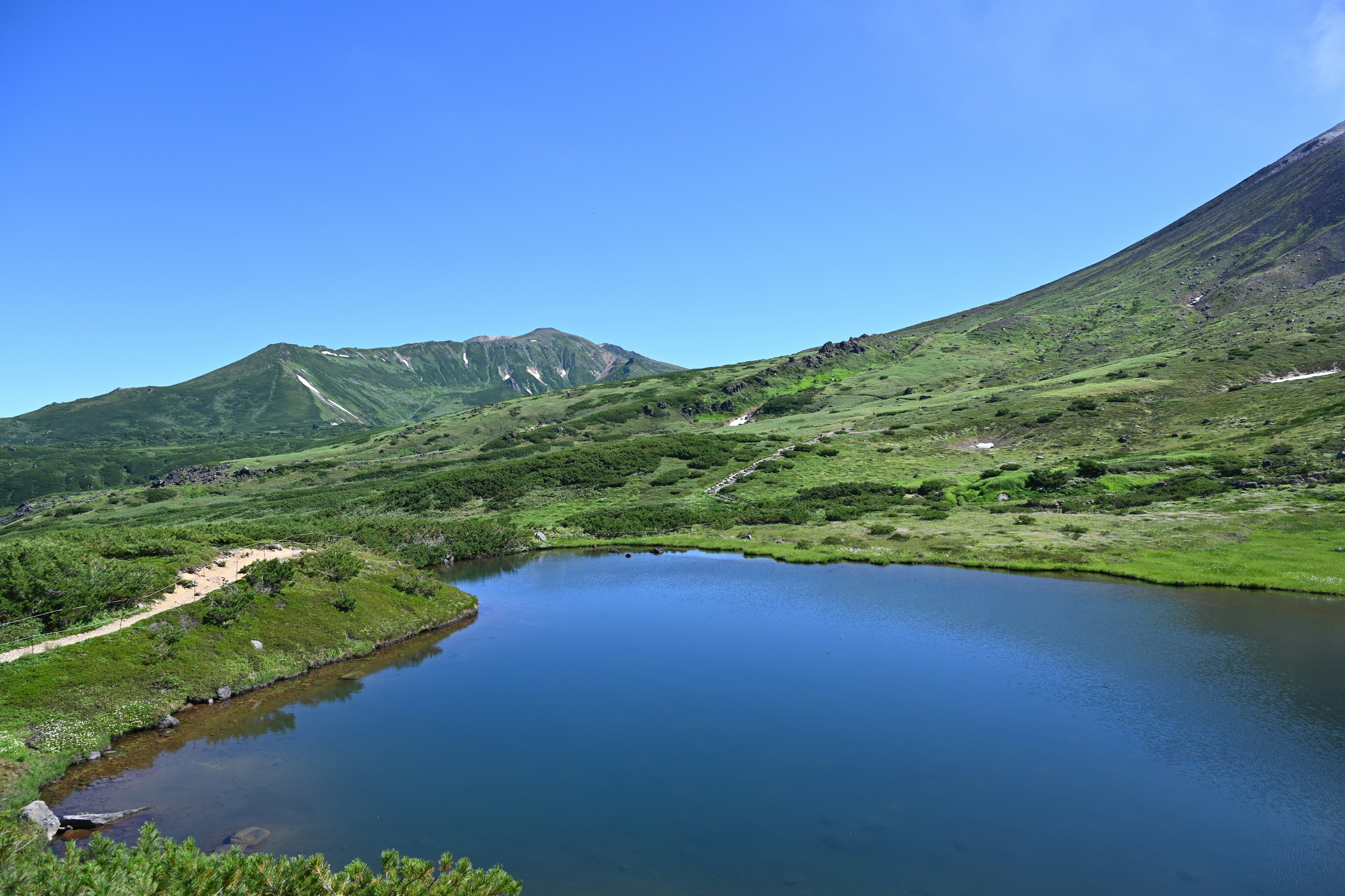 寧靜的湖泊景觀，四周環繞著綠色山脈和清澈的藍天