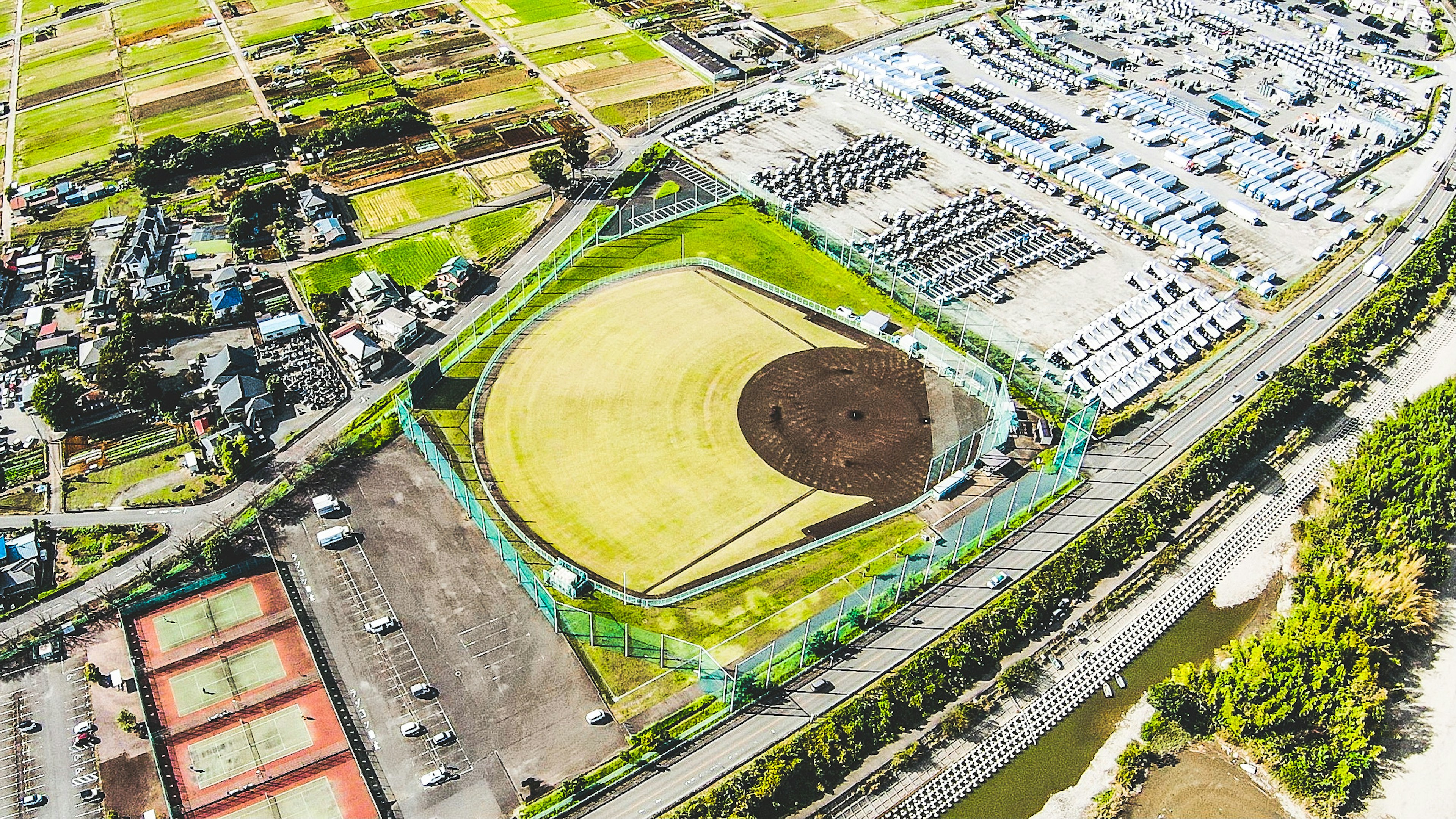 Aerial view of a baseball field surrounded by farmland parking lot and nearby residential areas