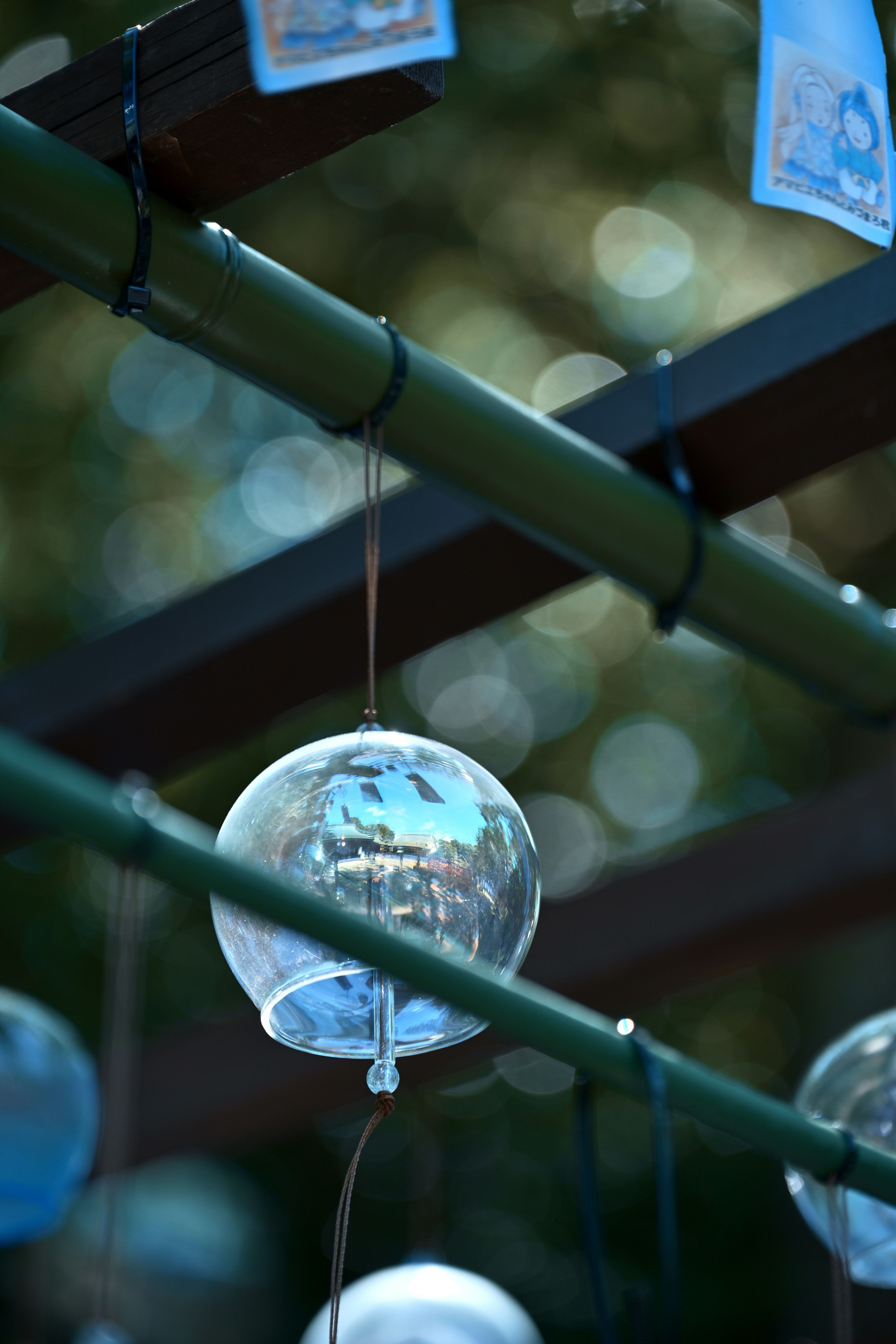 Clear wind chime hanging from bamboo with blurred green background