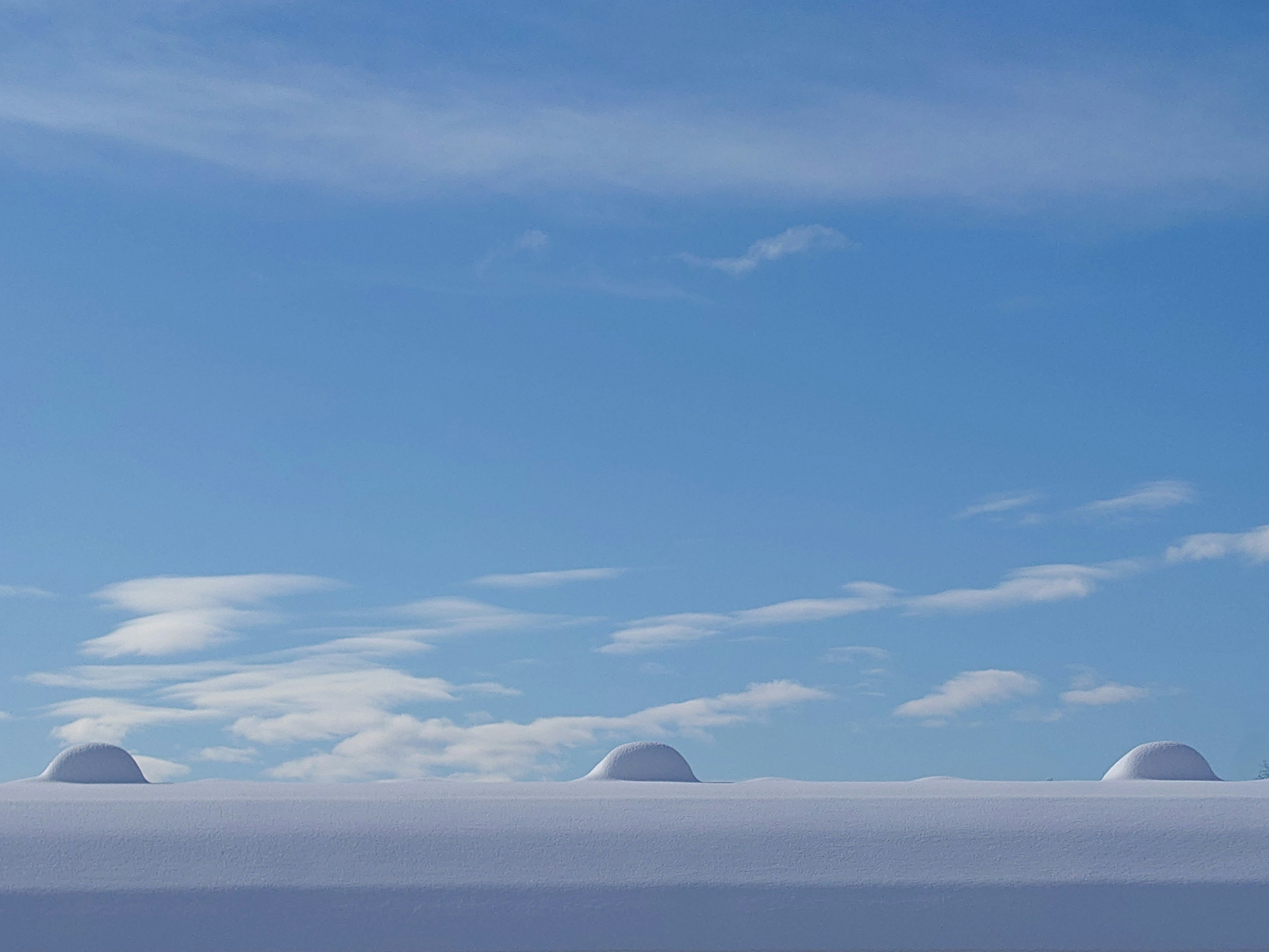 Snow-covered hill under a bright blue sky with white clouds