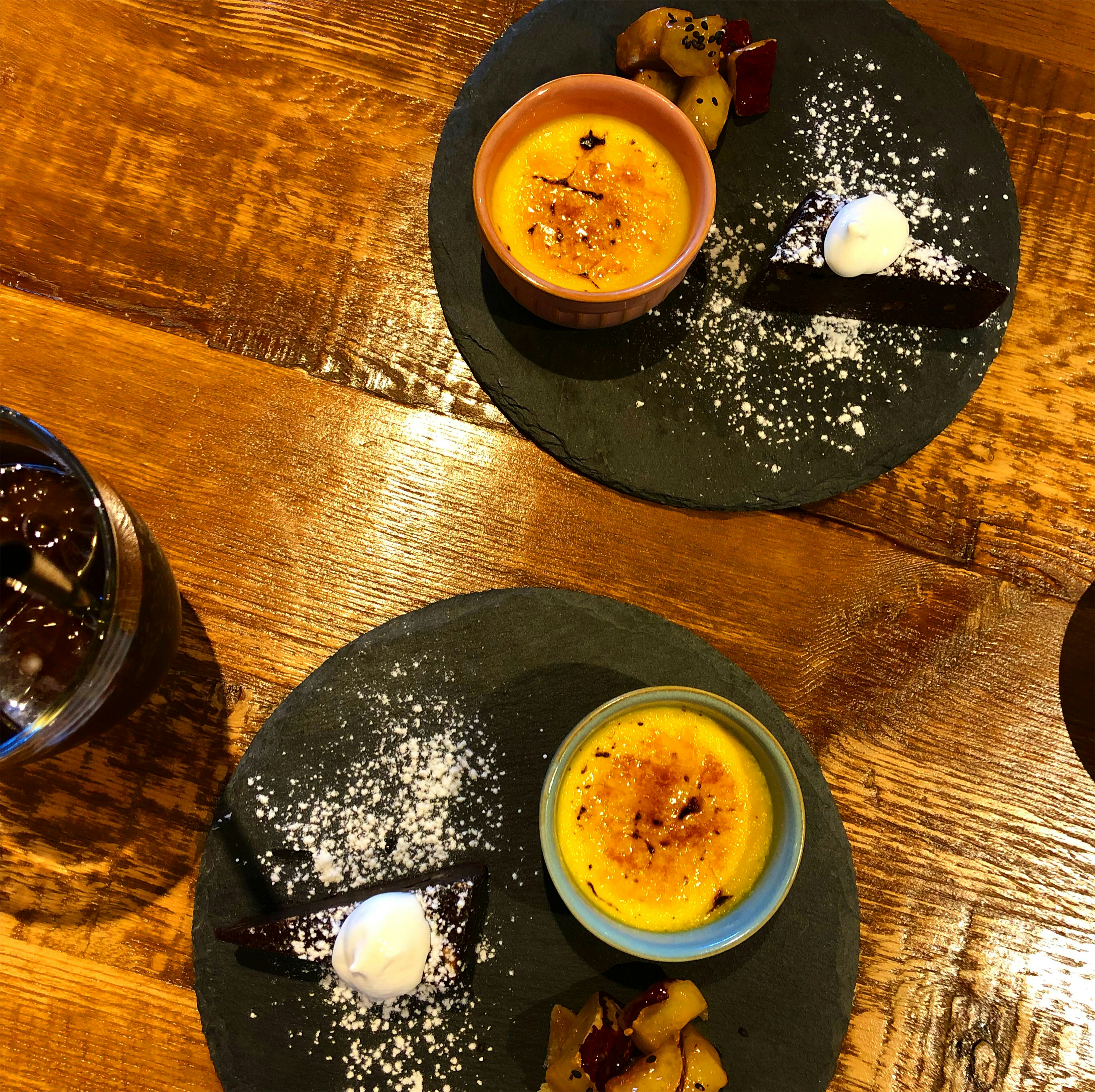 Dos platos de postre con crema pastelera cubierta de caramelo y decorada con crema batida y galletas