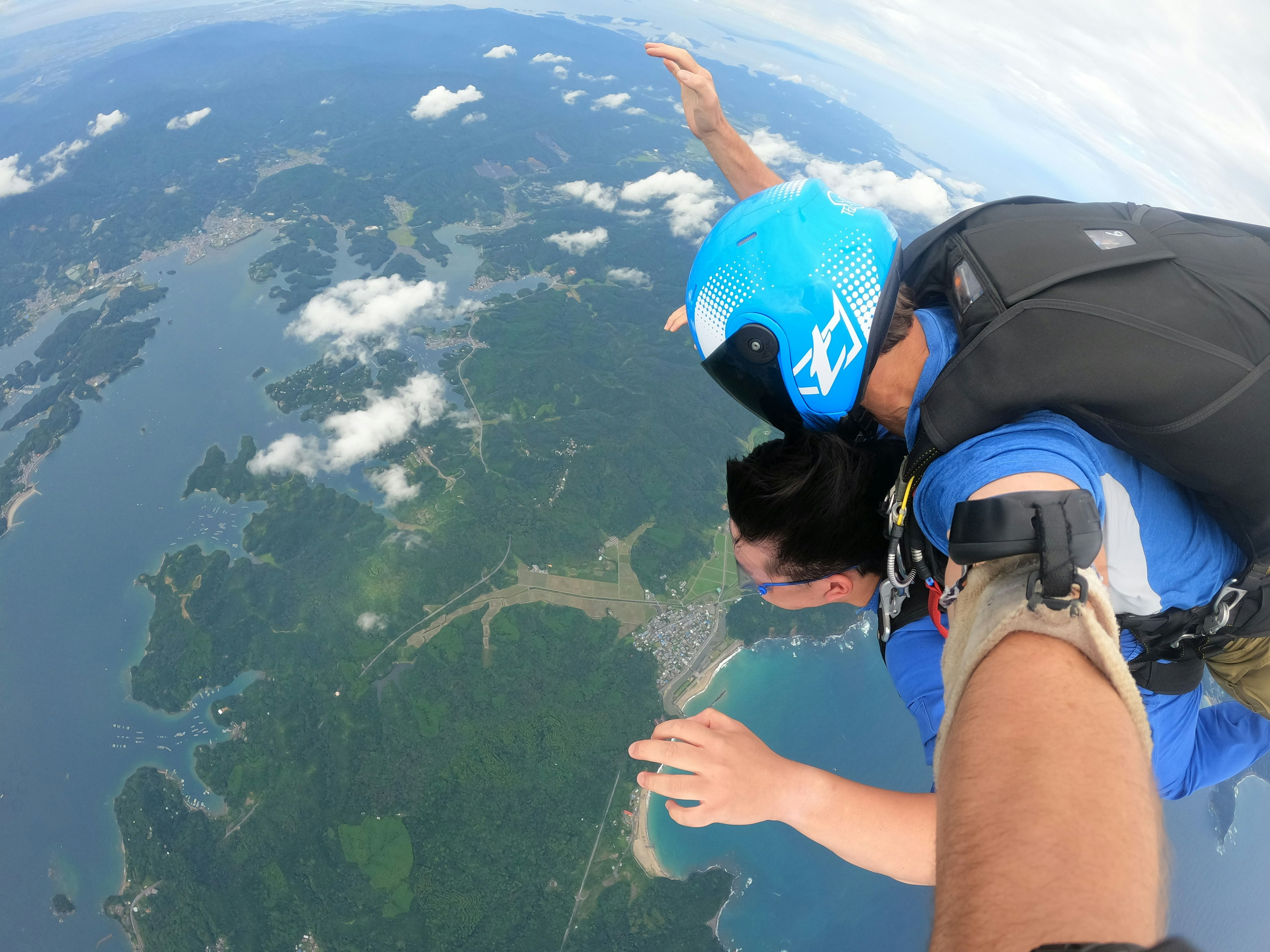 スカイダイビング中の二人の人物が空中での自由落下を楽しんでいる様子 風景には緑の島々と青い海が広がっている