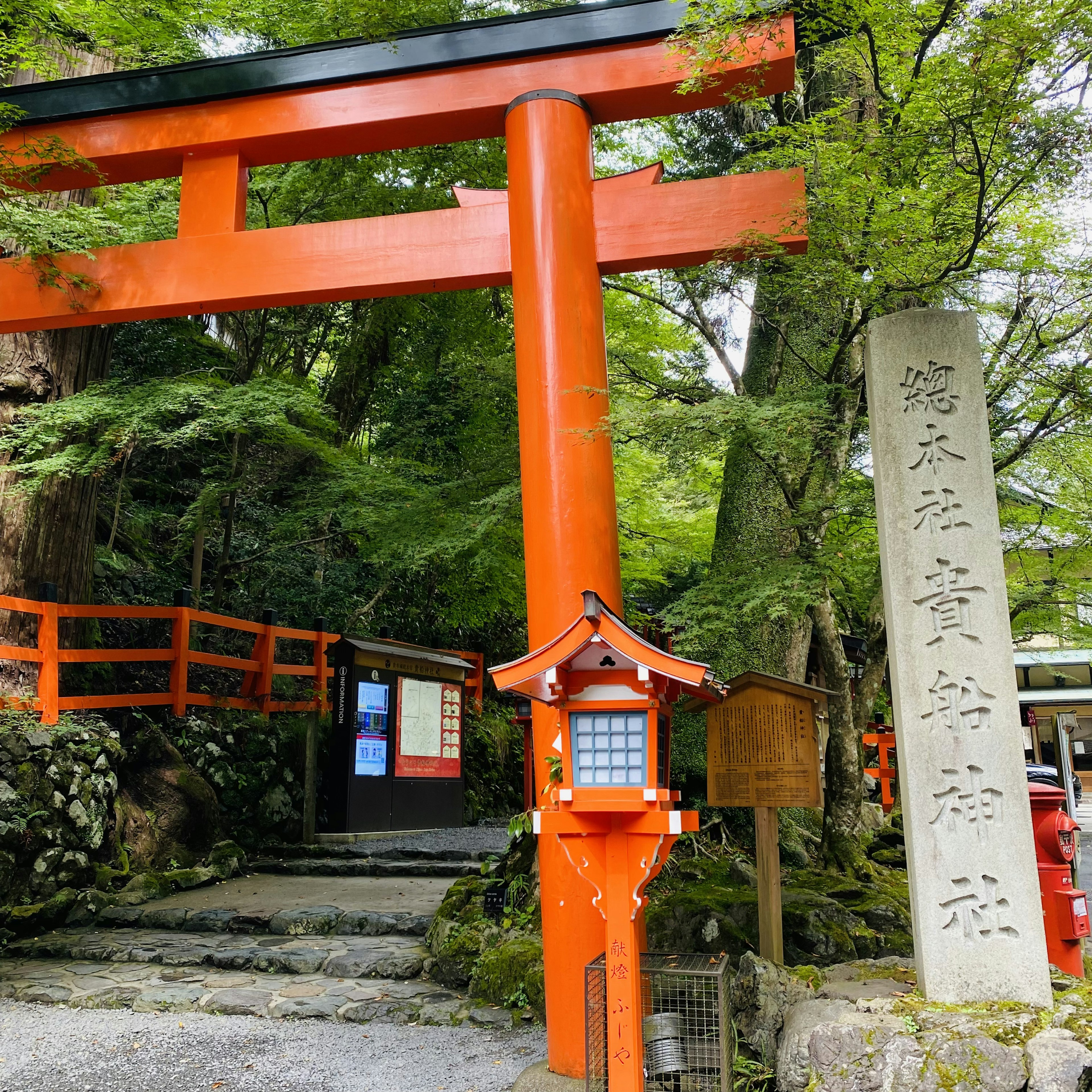 Lối vào một ngôi đền với cổng torii đỏ và bia đá được bao quanh bởi cây cối xanh tươi