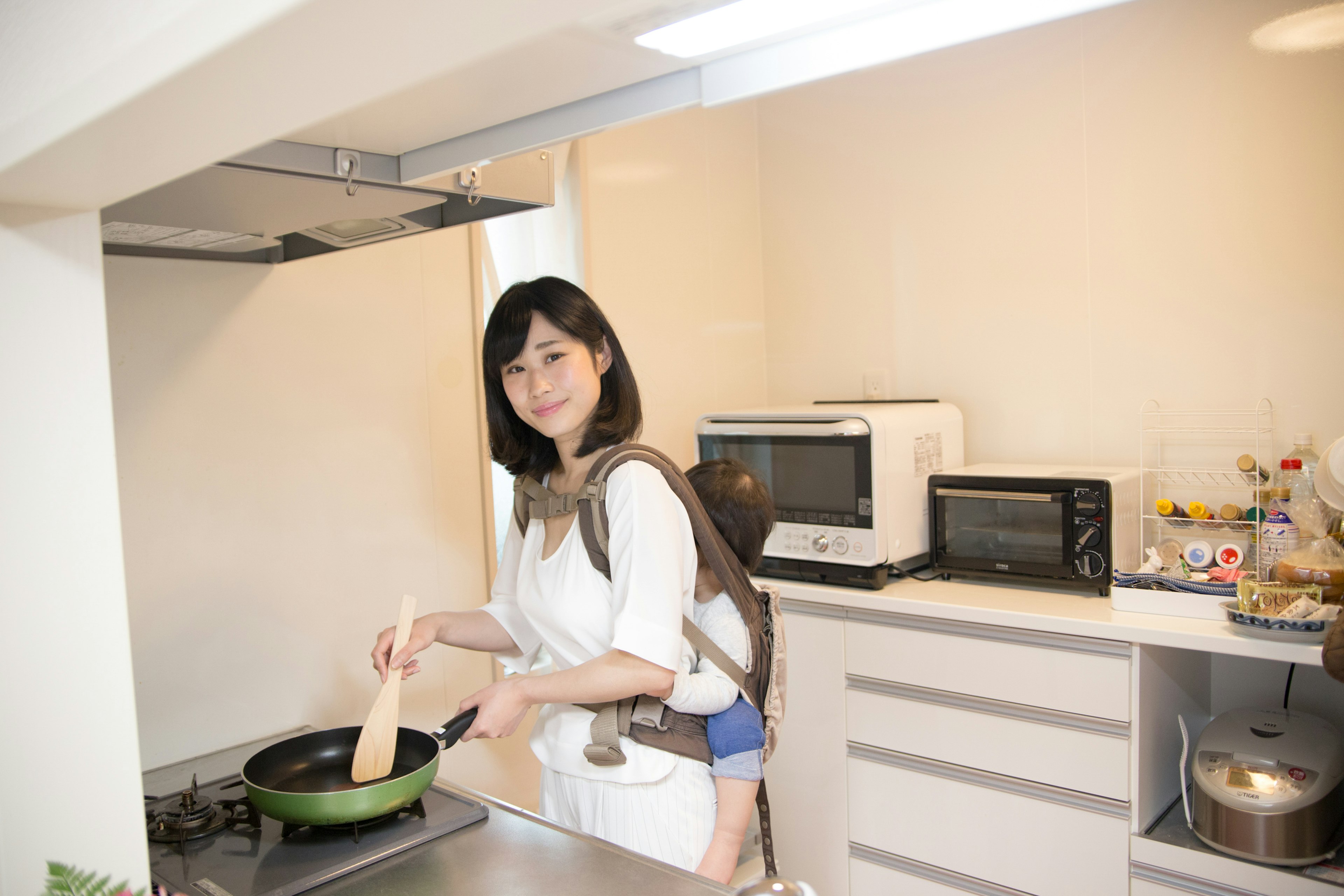 Wanita memasak di dapur tersenyum sambil memegang wajan