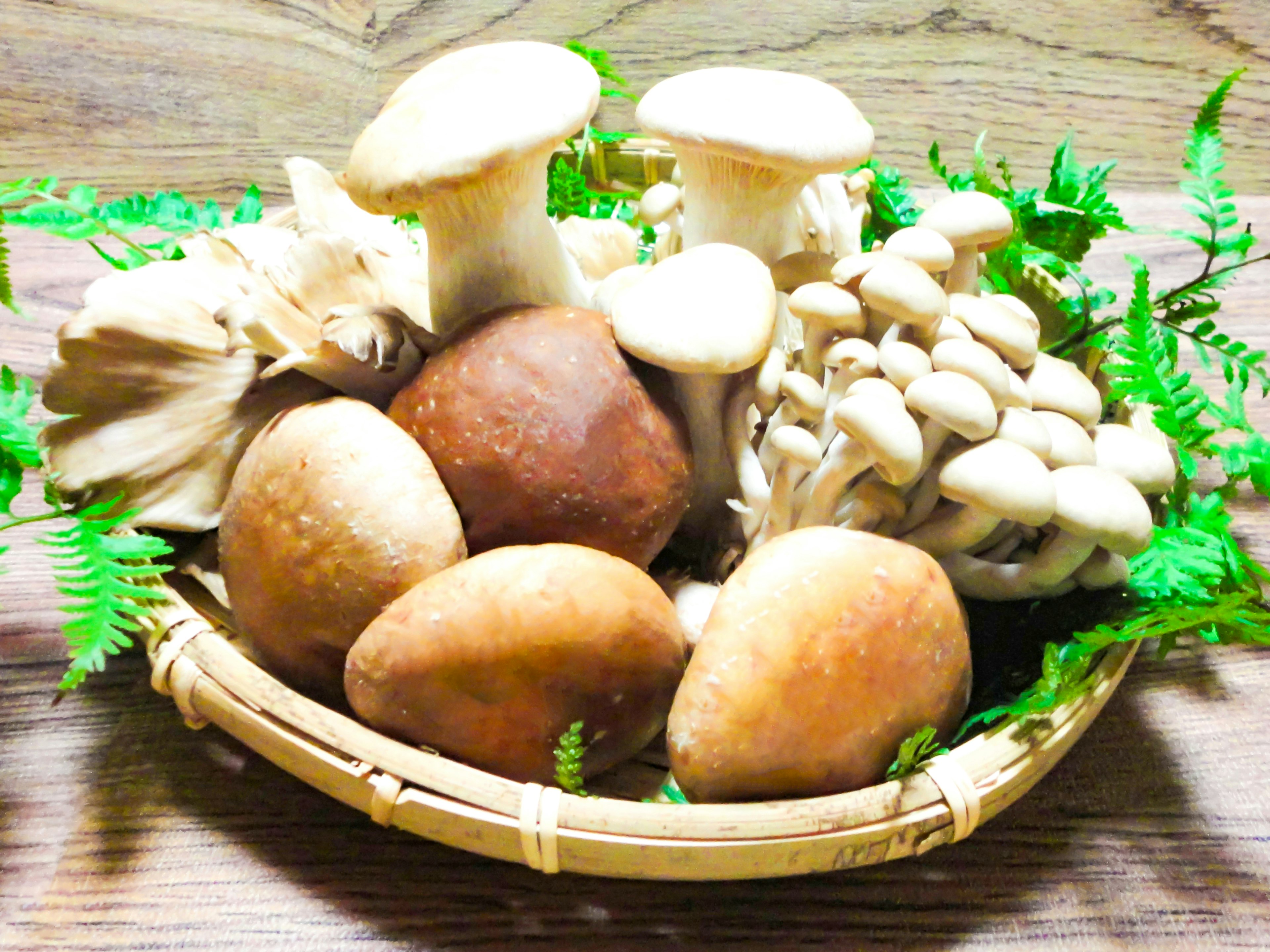 Various types of mushrooms arranged in a bamboo basket with green leaves