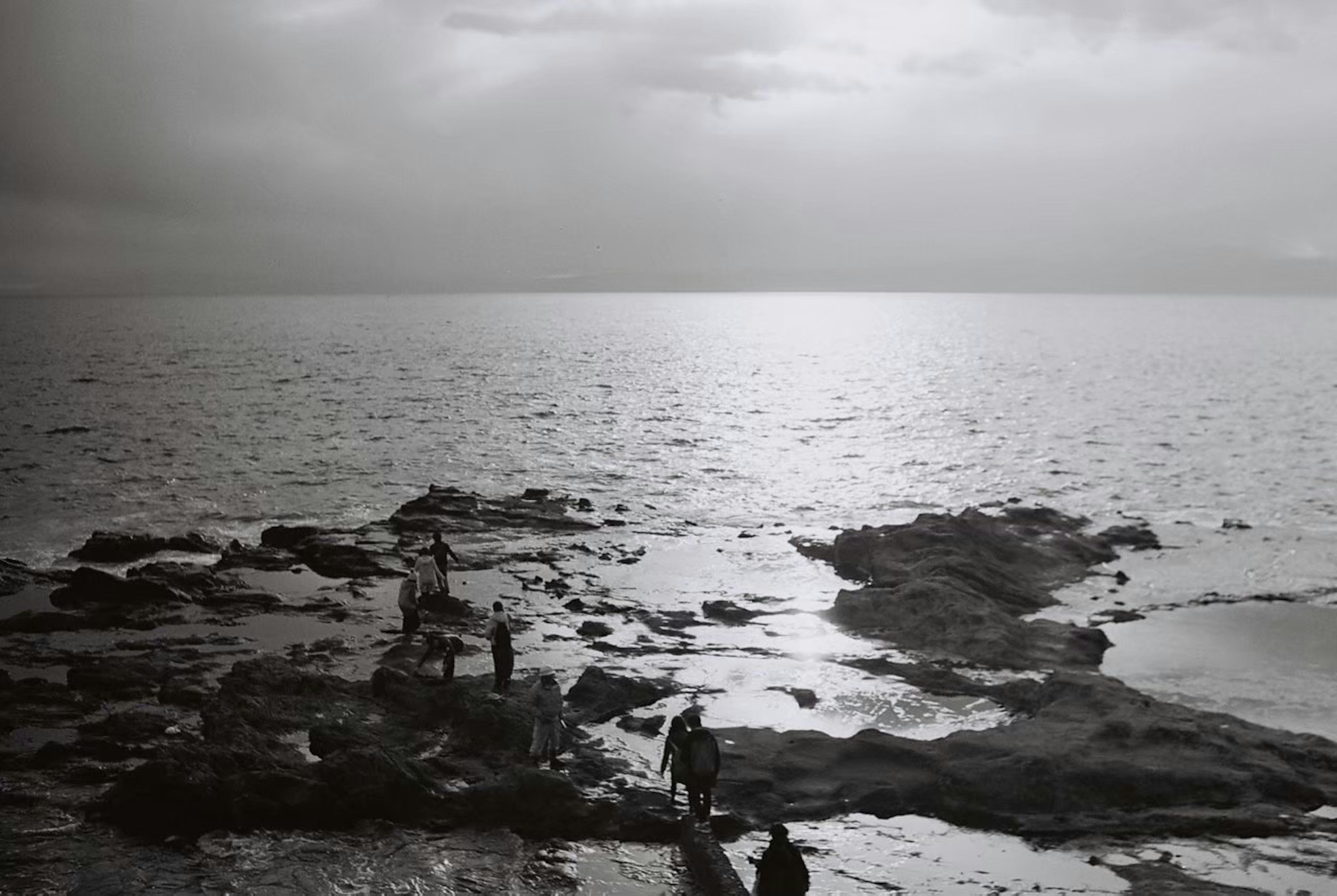 海岸で岩に立つ人々のモノクロ写真