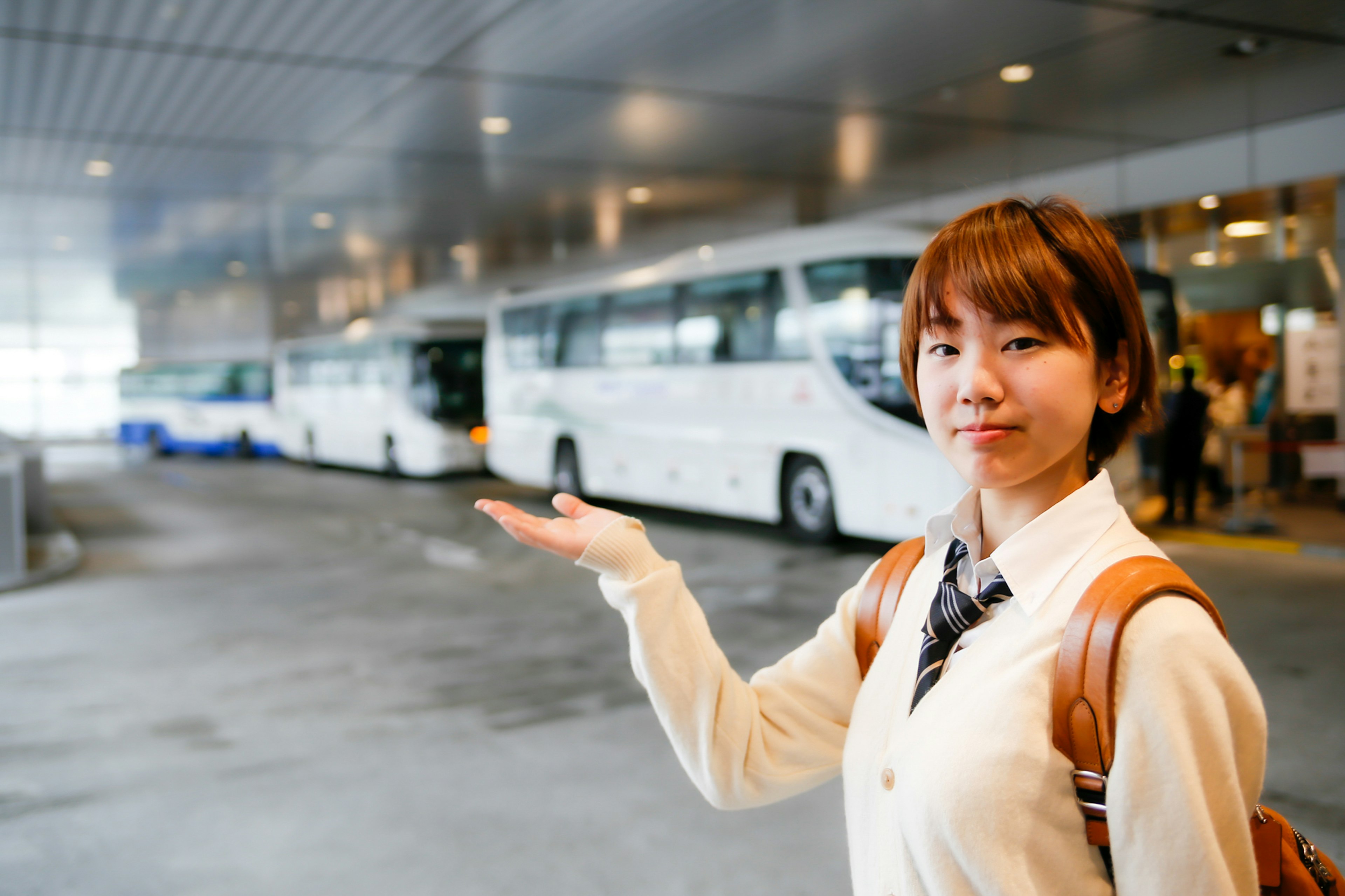 A woman pointing towards a row of white buses at a bus station