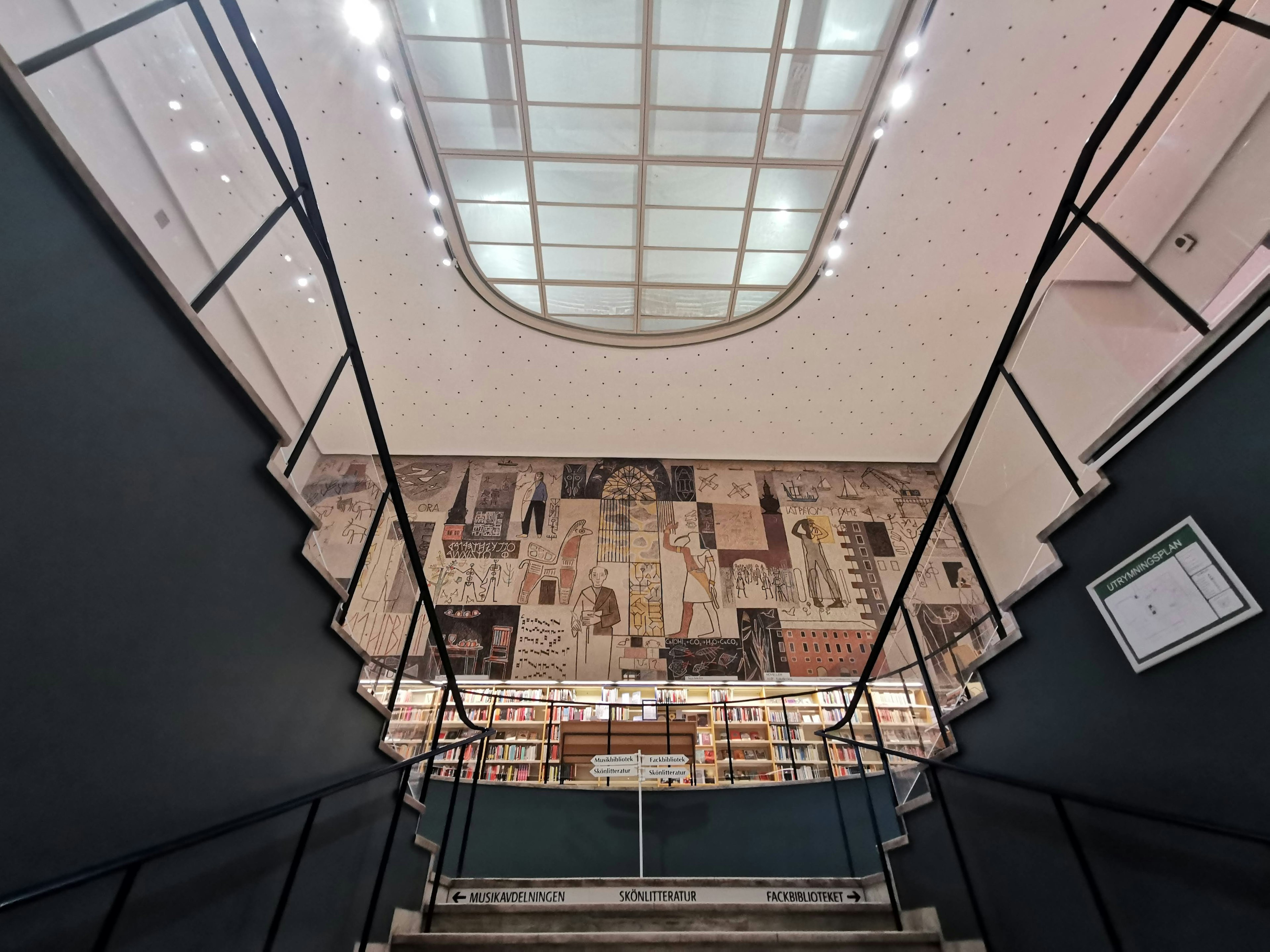 Vue de l'intérieur d'une bibliothèque depuis le bas d'un escalier Plafond large et lumineux Mur avec des fresques artistiques