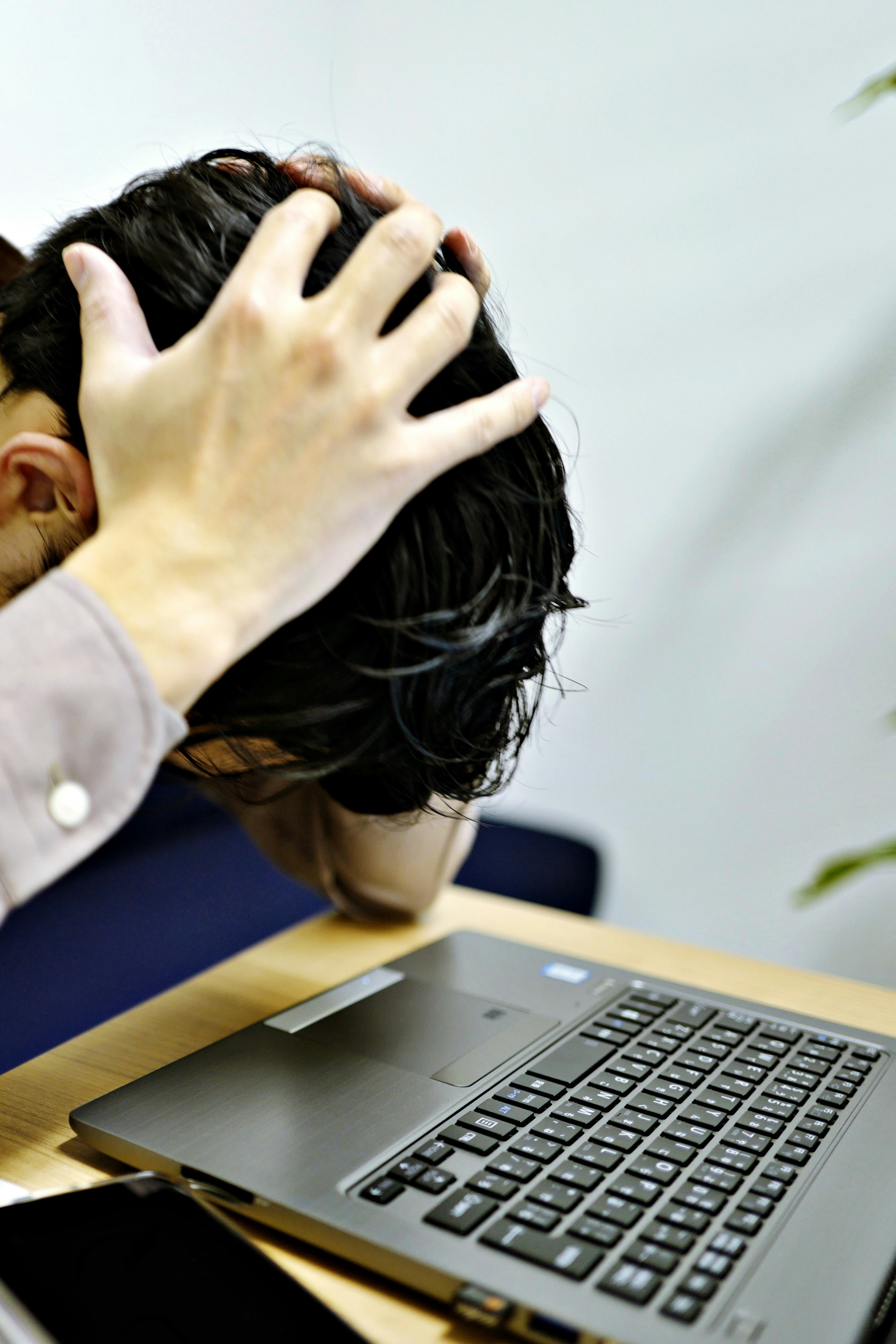 A man holding his head in front of a laptop