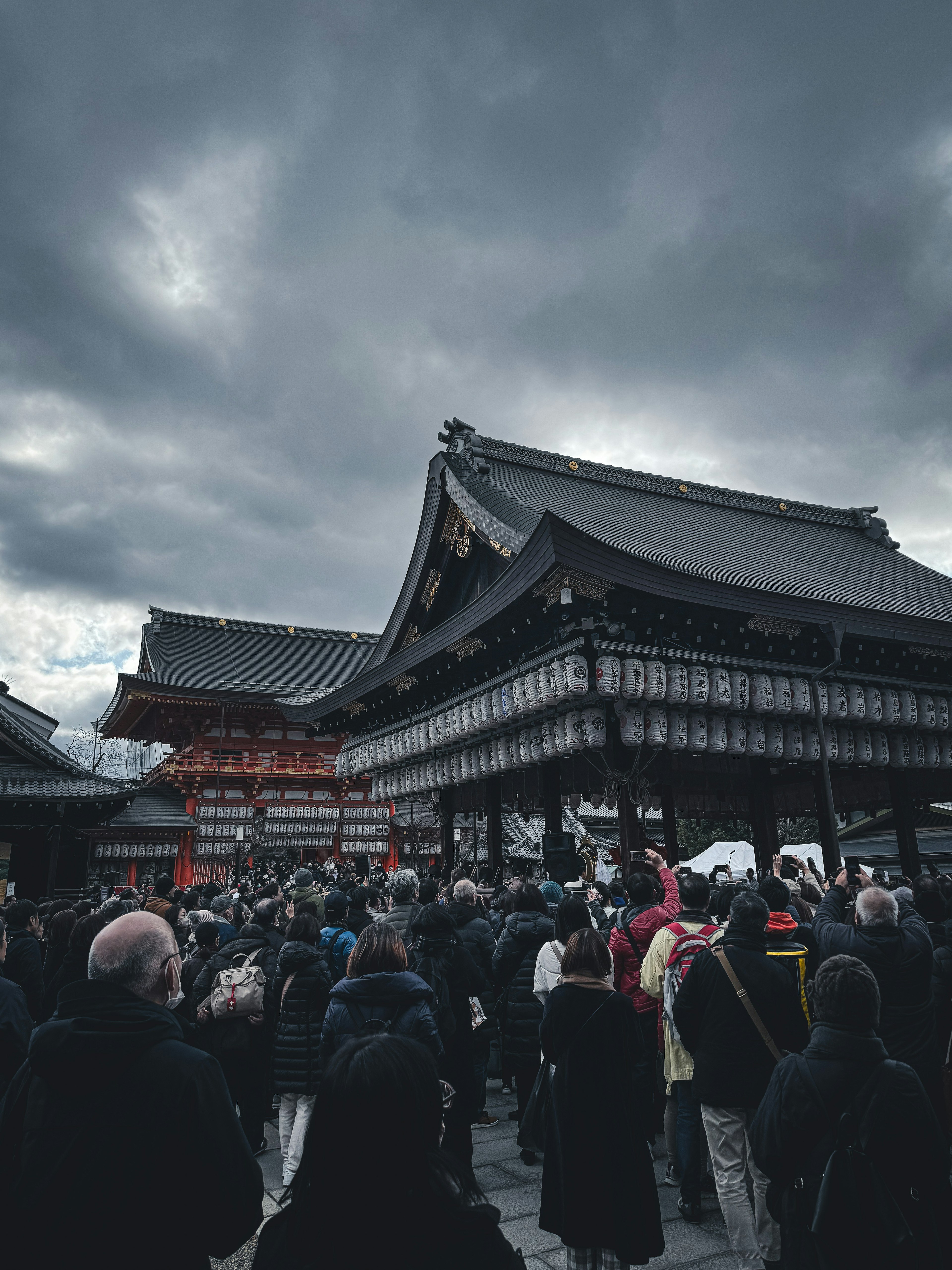 Menschenmenge vor einem traditionellen japanischen Tempel unter dunklen Wolken