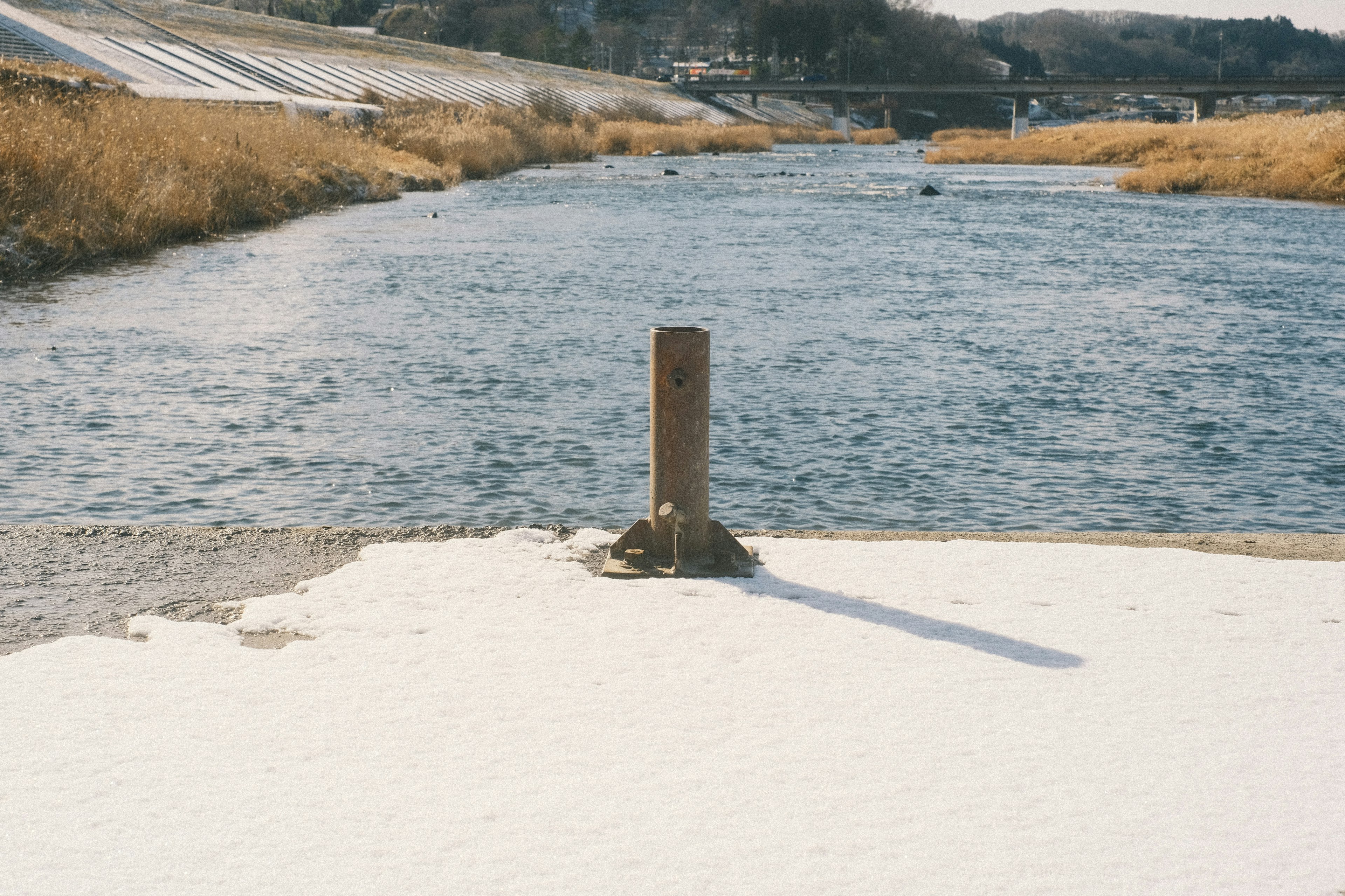 雪覆蓋的河岸上有一根木柱和流動的水