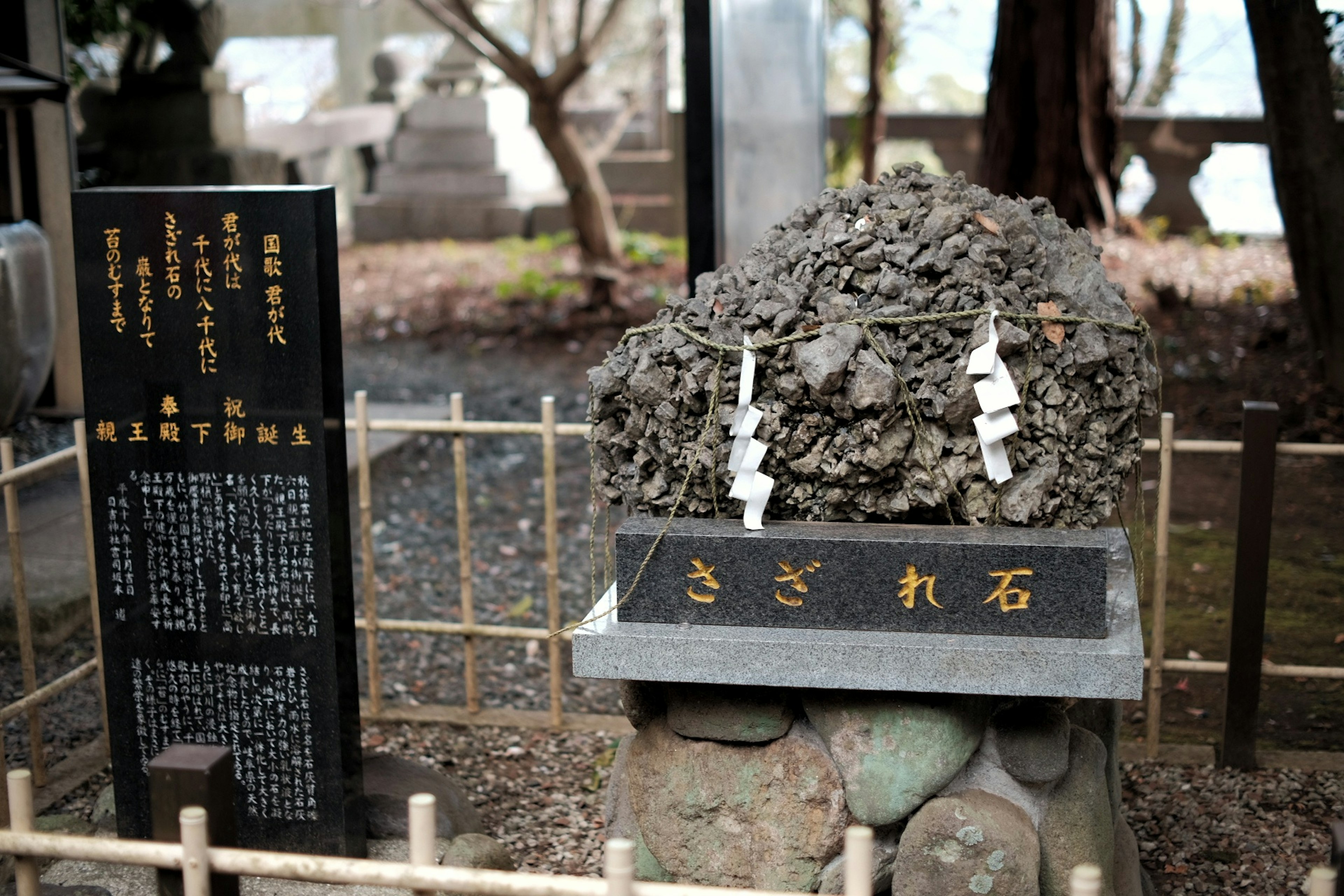 神社の石碑で、周囲には竹のフェンスと説明板がある