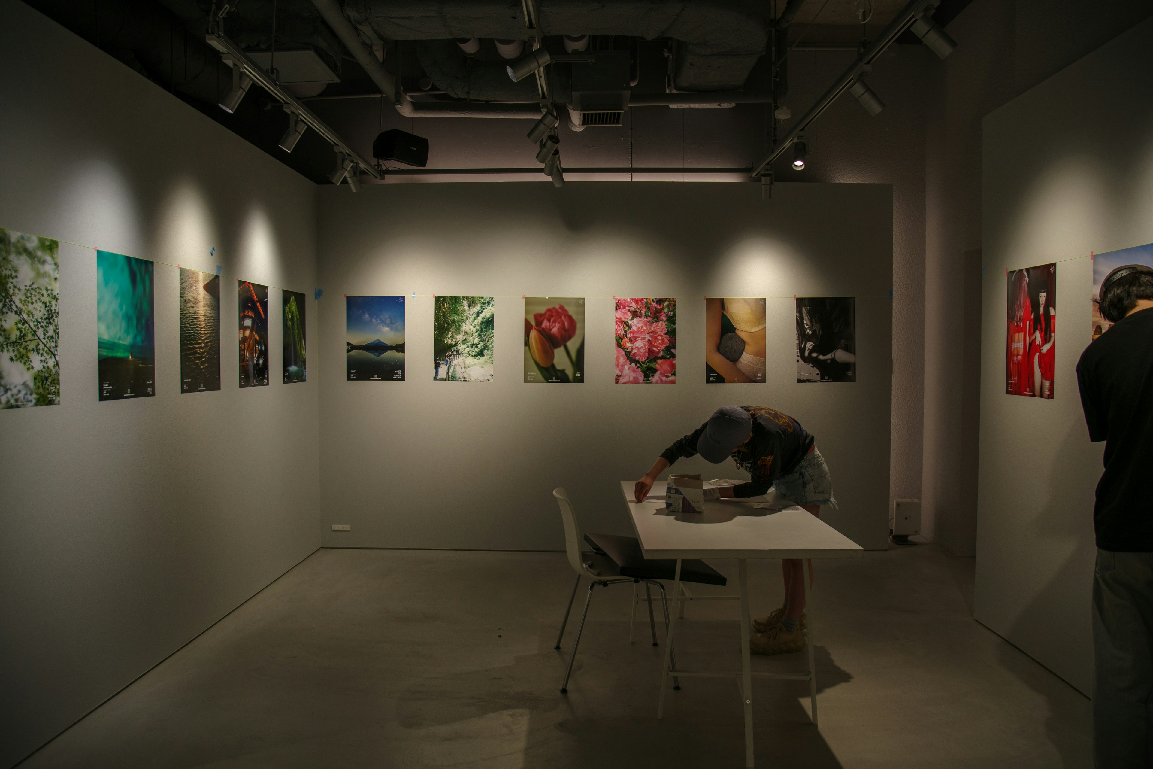 Interior galeri seni dengan foto-foto yang dipajang di dinding dan seseorang yang bekerja di meja