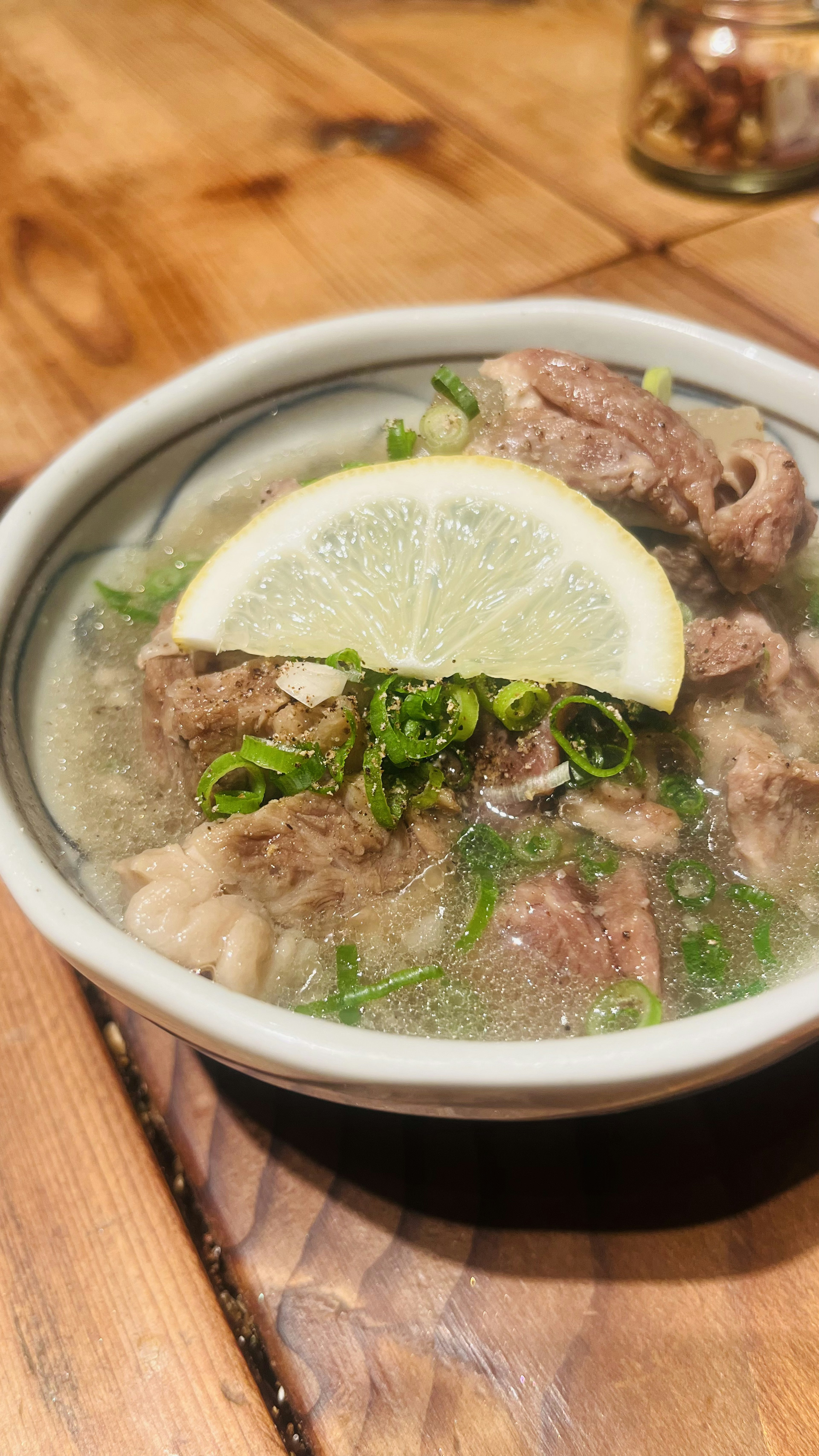 Bowl of soup with meat topped with lime slice and herbs