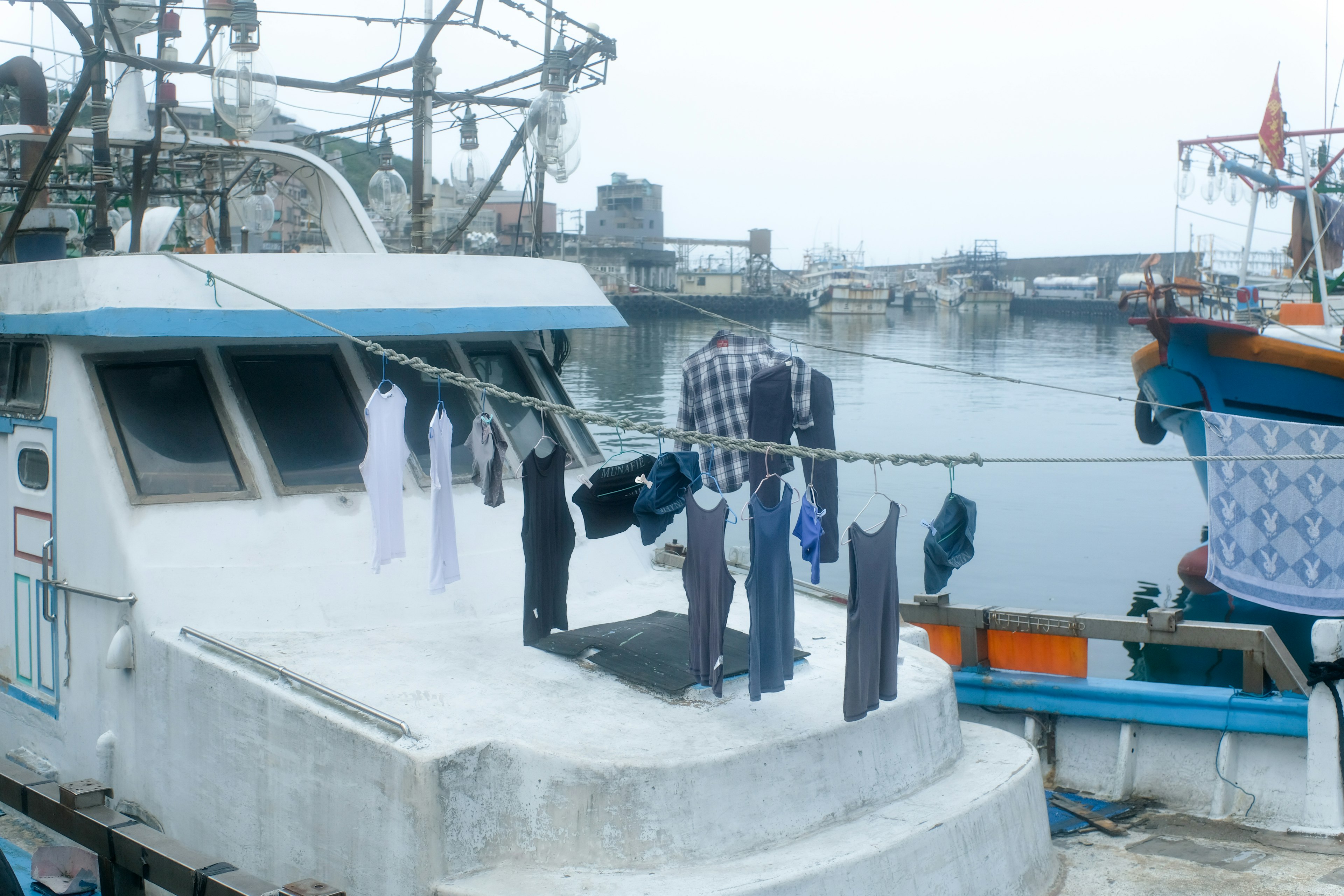 Kleidung, die auf dem Deck eines Fischerboots hängt, mit Blick auf den Hafen im Hintergrund