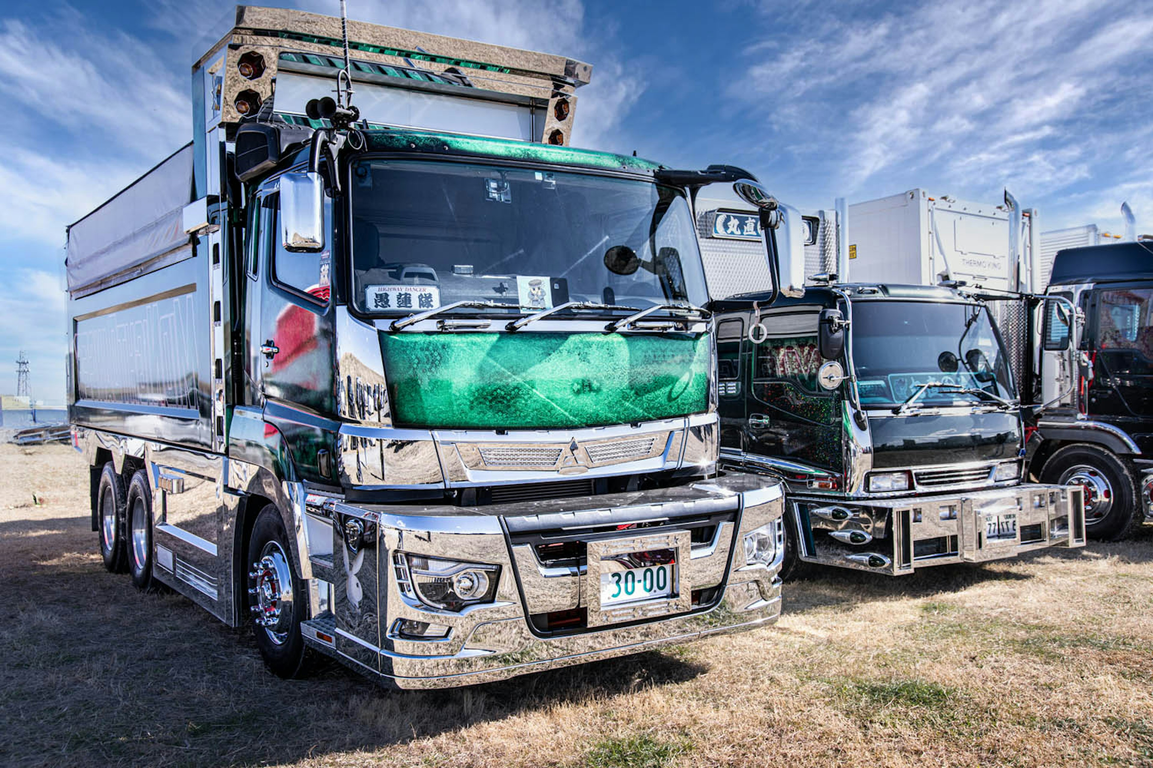 Sebuah truk hijau diparkir di bawah langit biru Truk lain terlihat di dekatnya